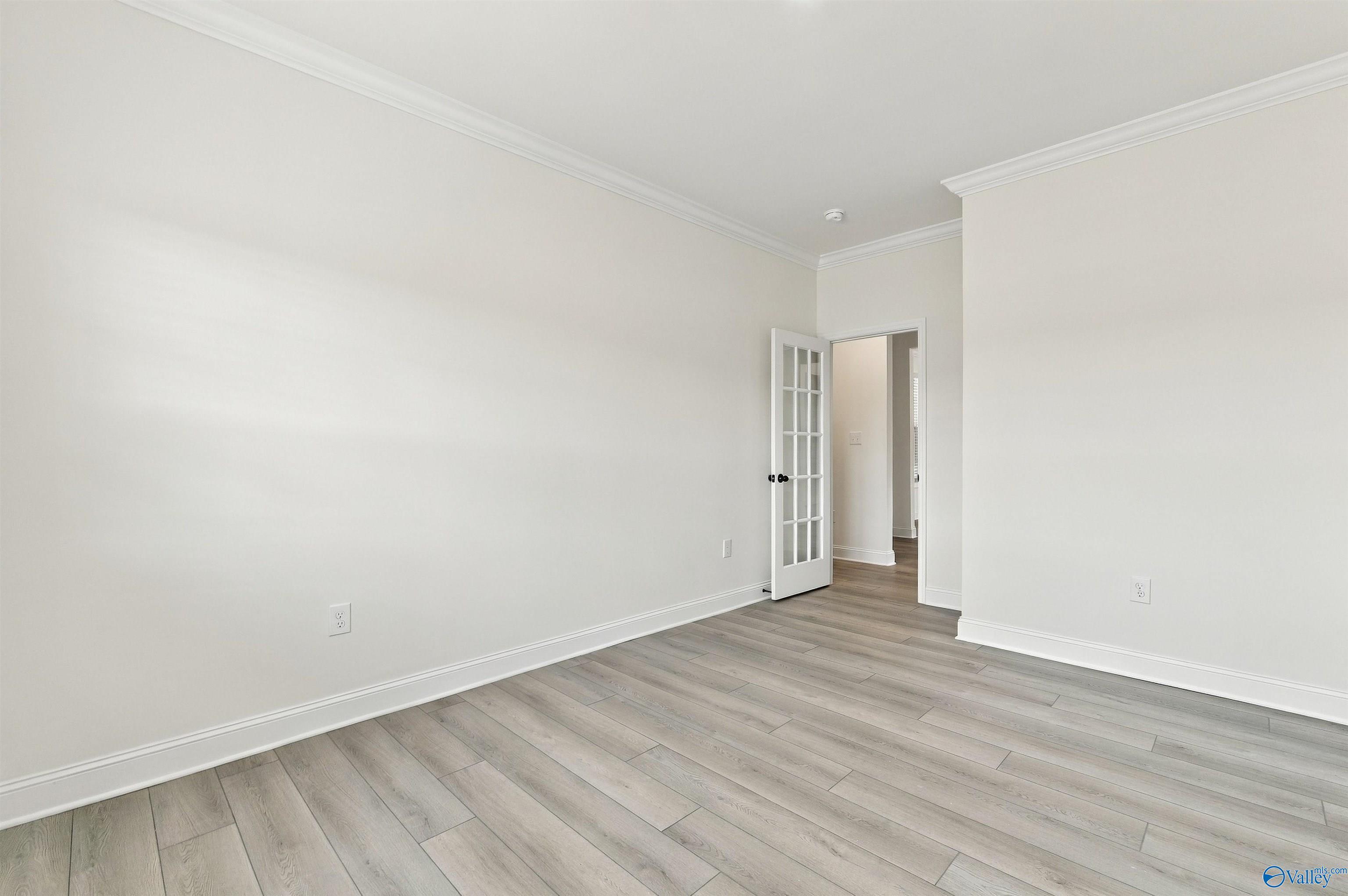 Empty room with gray wood-look flooring, white walls, and French door in Davidson Homes Valencia floor plan, Huntsville, Alabama