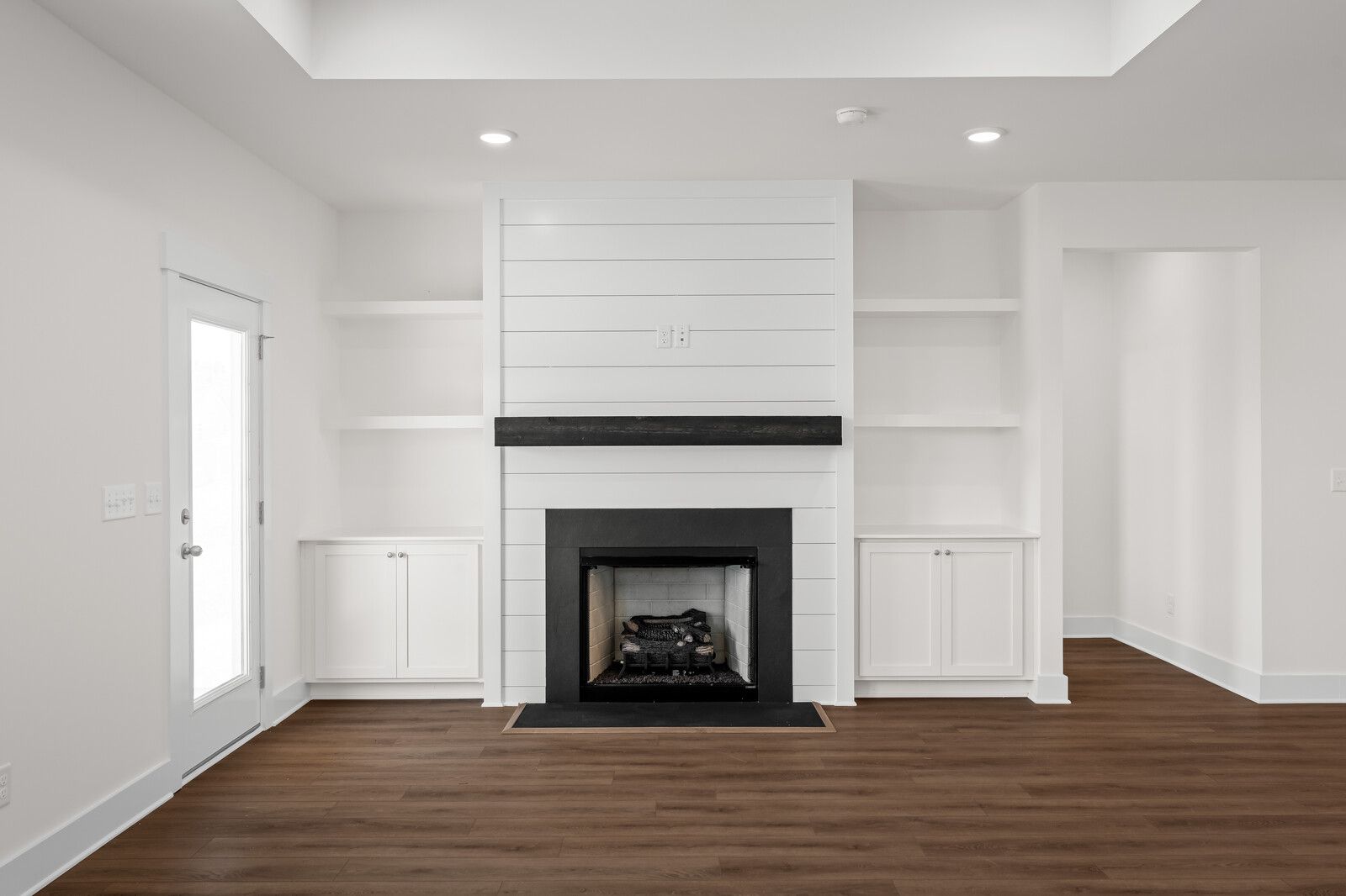 Living room fireplace in The Cottonwood featuring shiplap detail, a dark wood mantel, and built-in shelving.