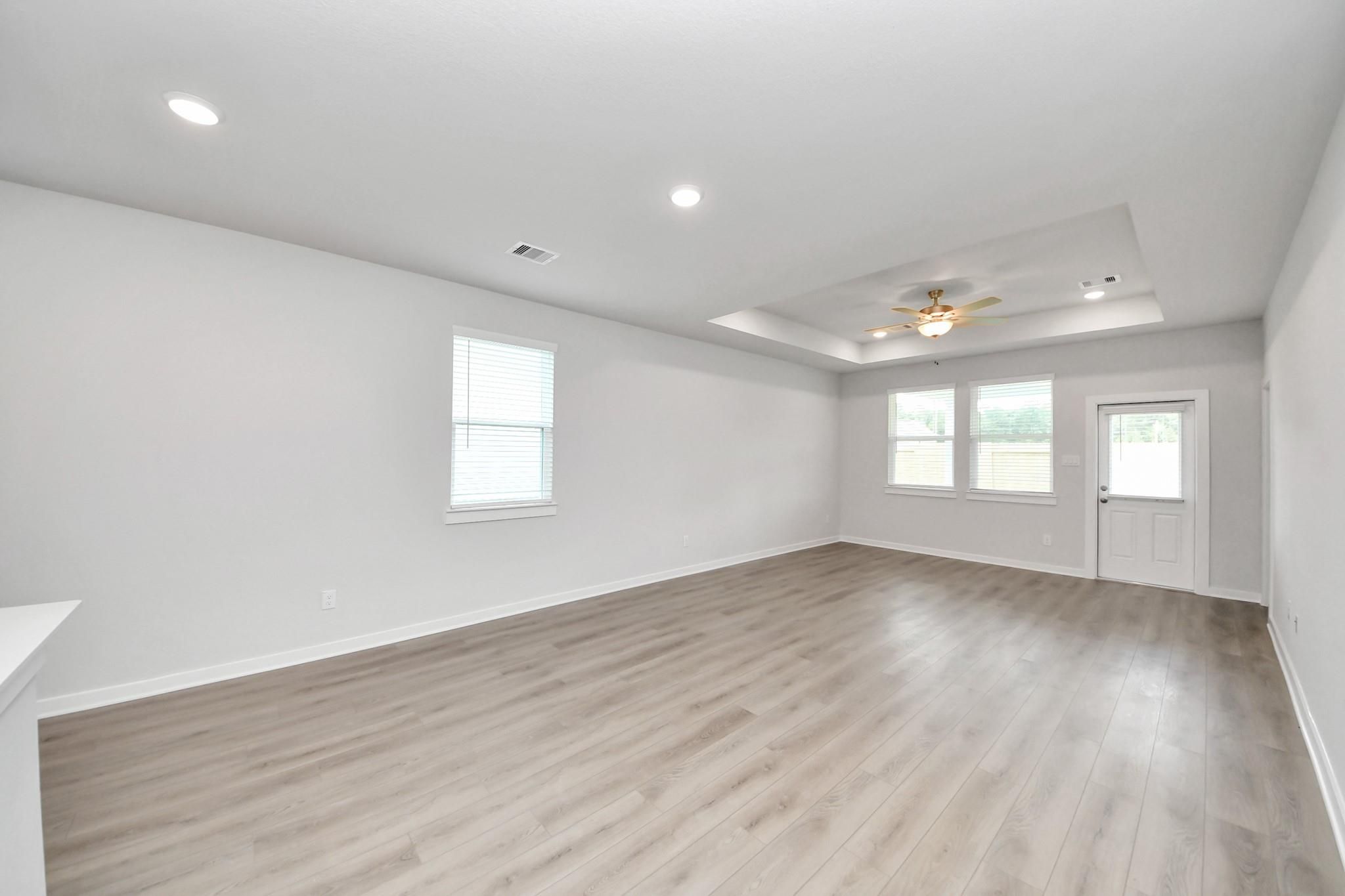 Spacious living room with tray ceiling and wood-style flooring in Davidson Homes The Frio F floor plan, Cleveland, Texas.