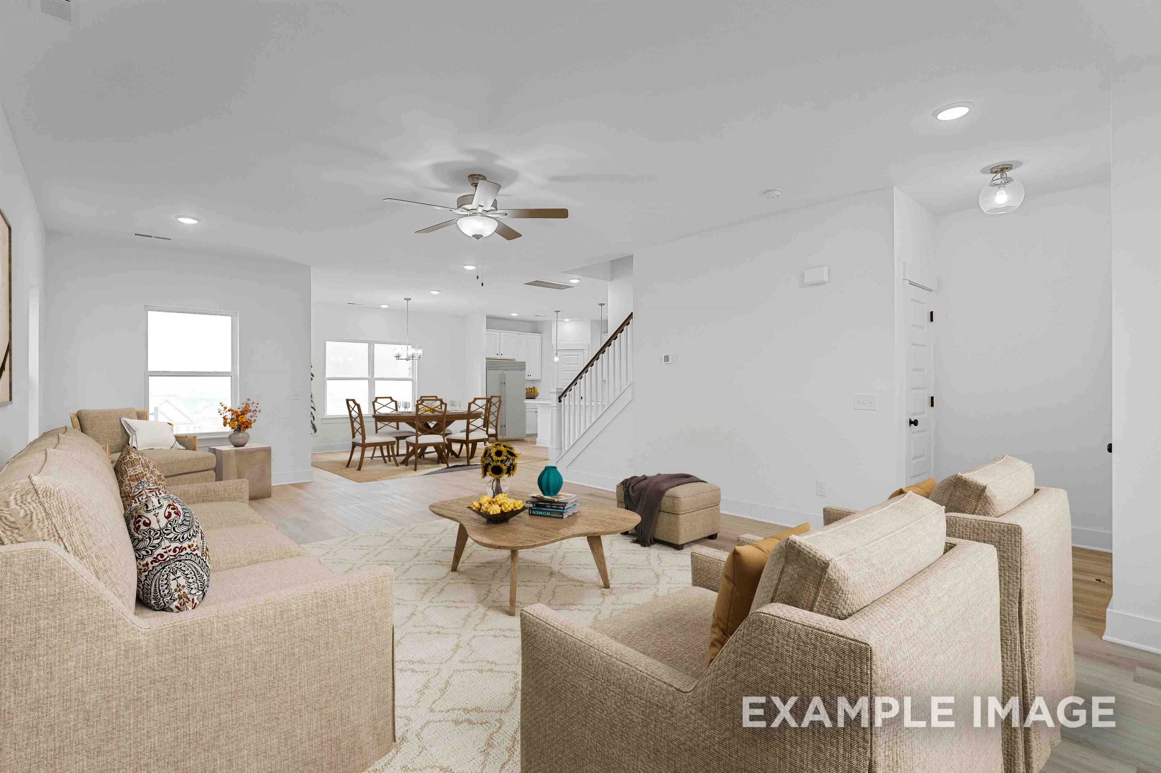 Open-concept living and dining area in The Charleston home design with beige sofas, wooden coffee table, staircase, and large windows