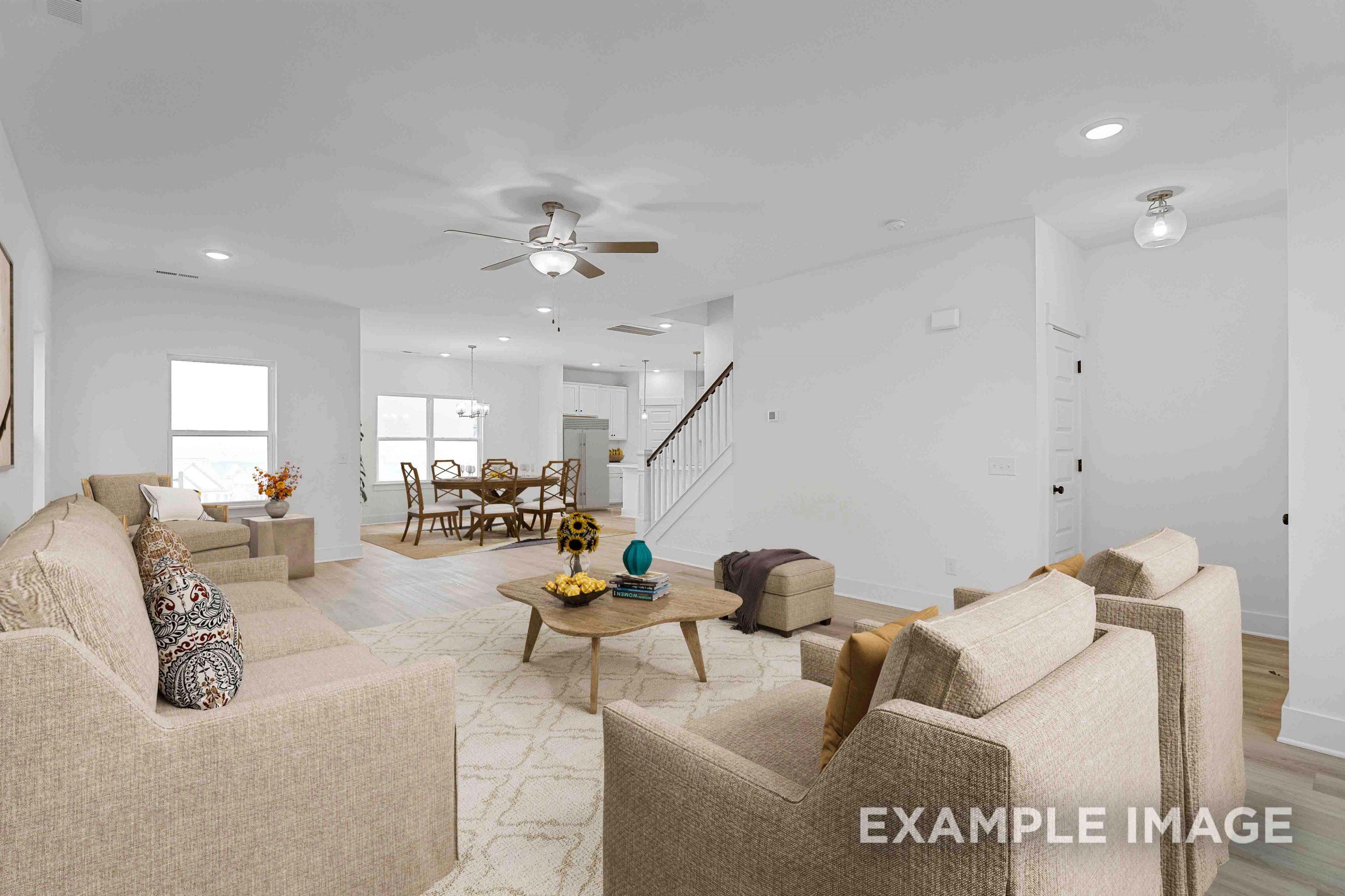 Open-concept living and dining area in The Charleston home design with beige sofas, wooden coffee table, staircase, and large windows