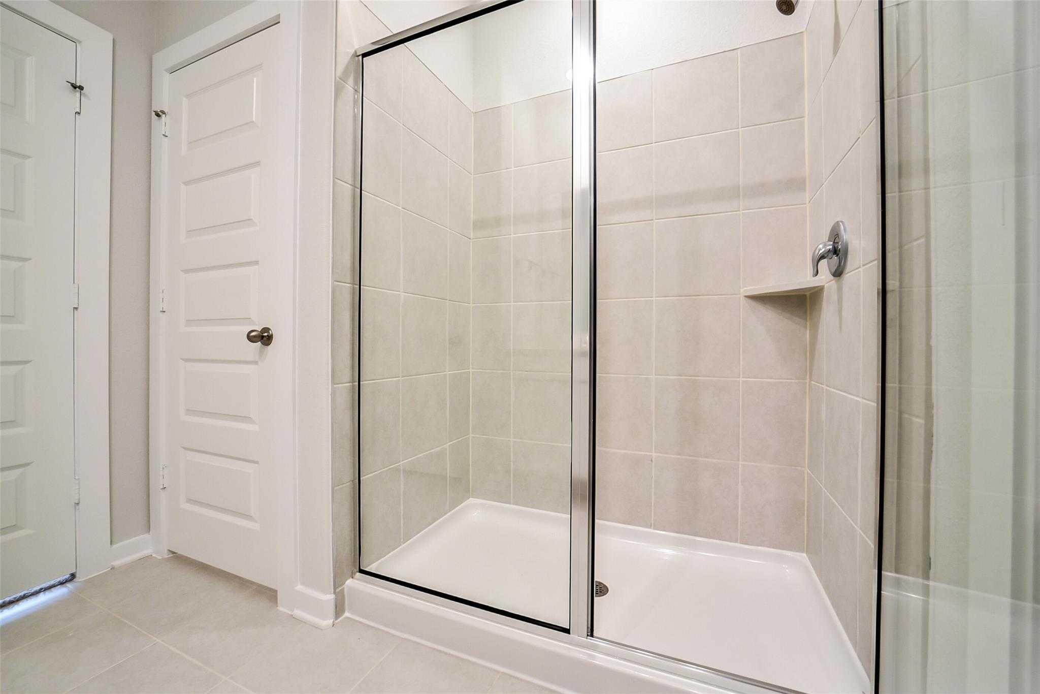 Modern walk-in shower with frameless glass door, white subway tiles, and built-in shelf in master bath, The Blanco E, Davidson Homes, Magnolia, Texas