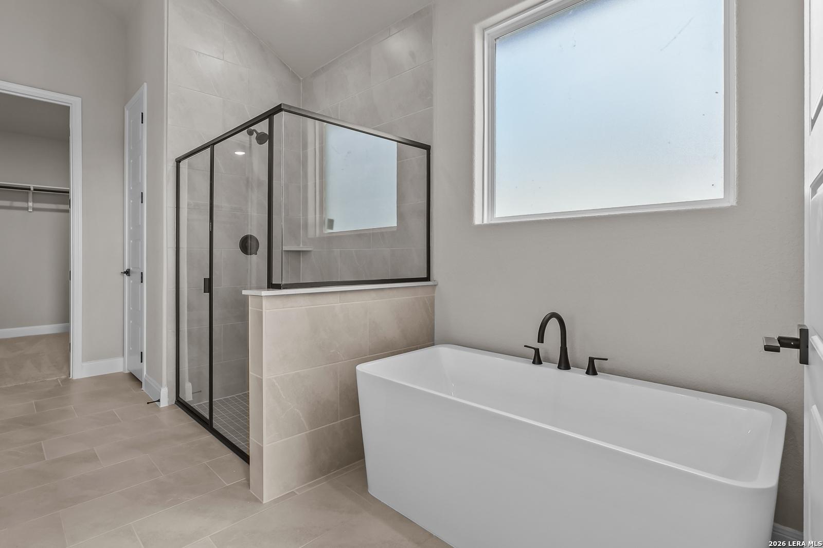 Freestanding soaking tub and glass walk-in shower in master bathroom of Davidson Homes The Foster E in Castroville, Texas