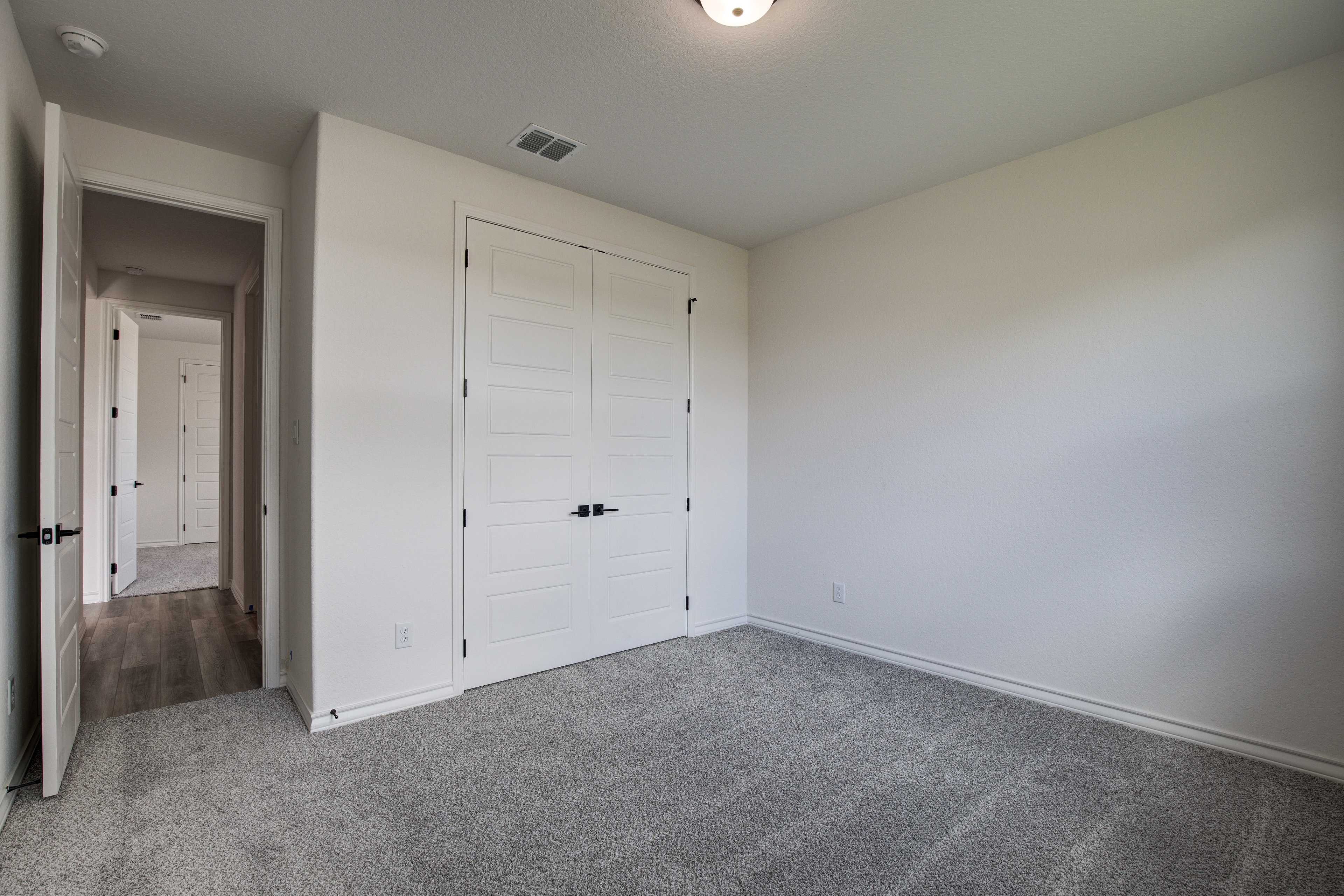 Spacious bedroom in The Lanier featuring white walls, gray carpet, double closet doors, and hallway access