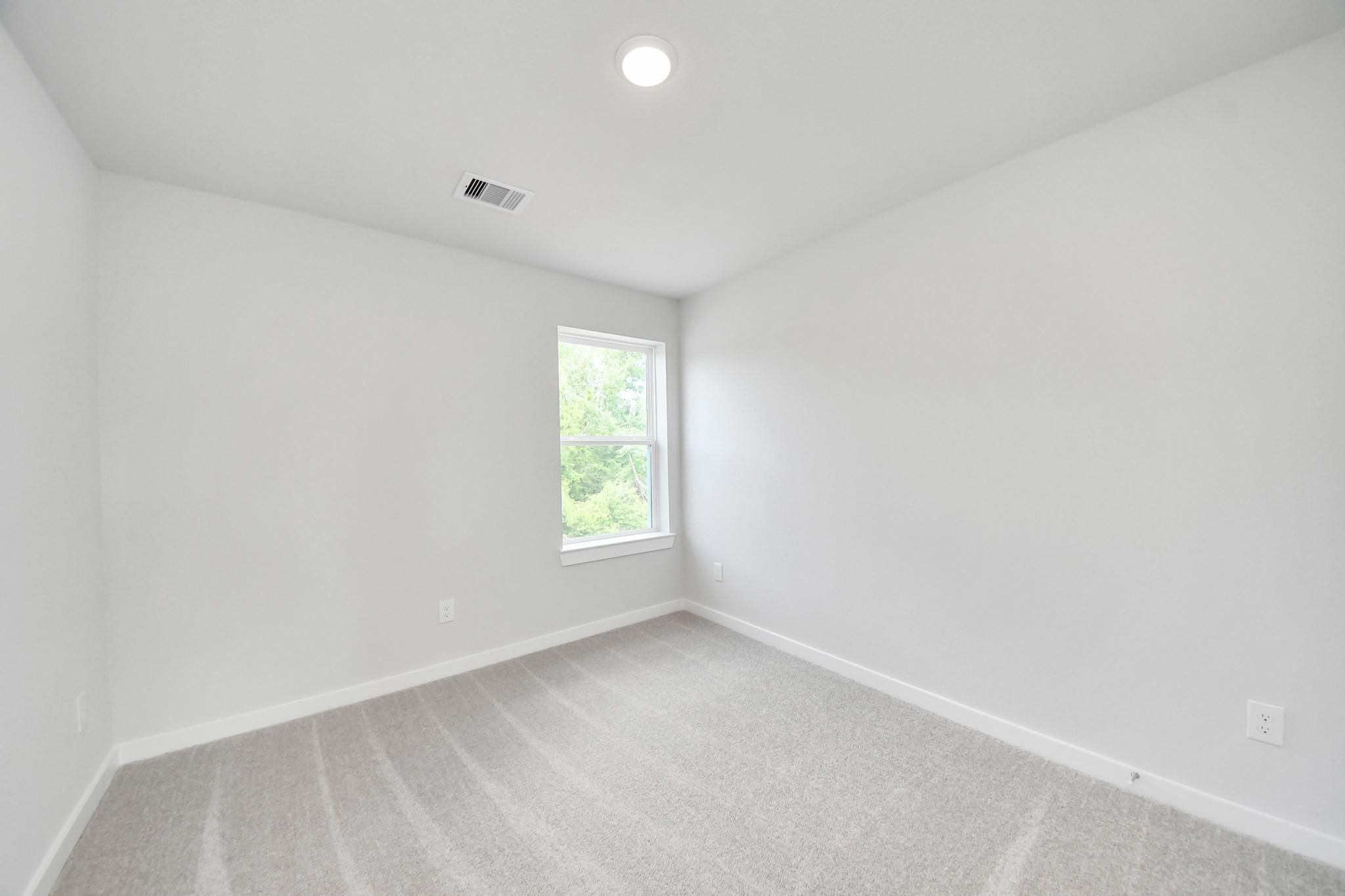 Bright, neutral secondary bedroom with plush carpet in The Blanco E floor plan at Caney Creek Place, Conroe, Texas.