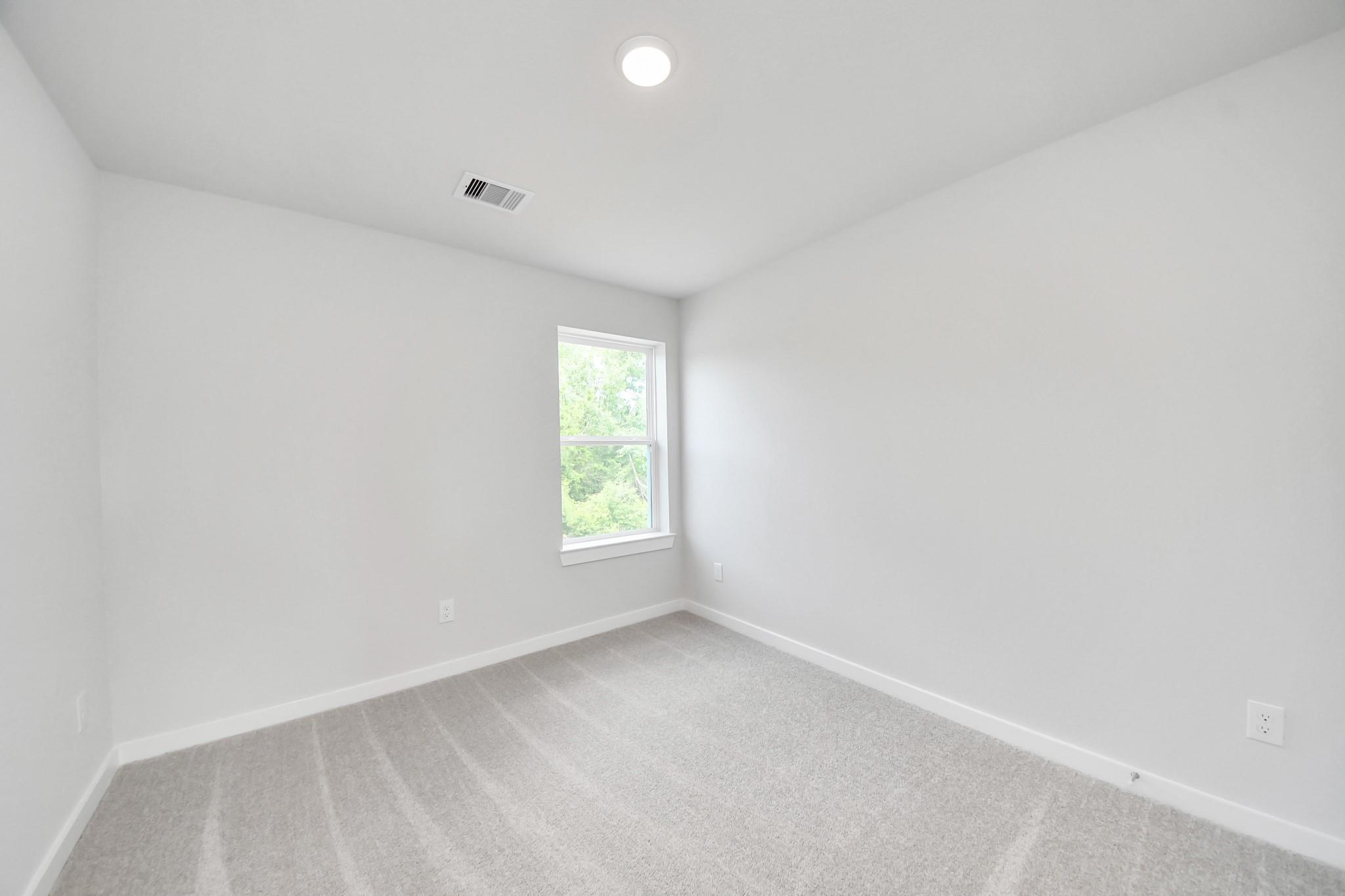 Bright, neutral secondary bedroom with plush carpet in The Blanco E floor plan at Caney Creek Place, Conroe, Texas.