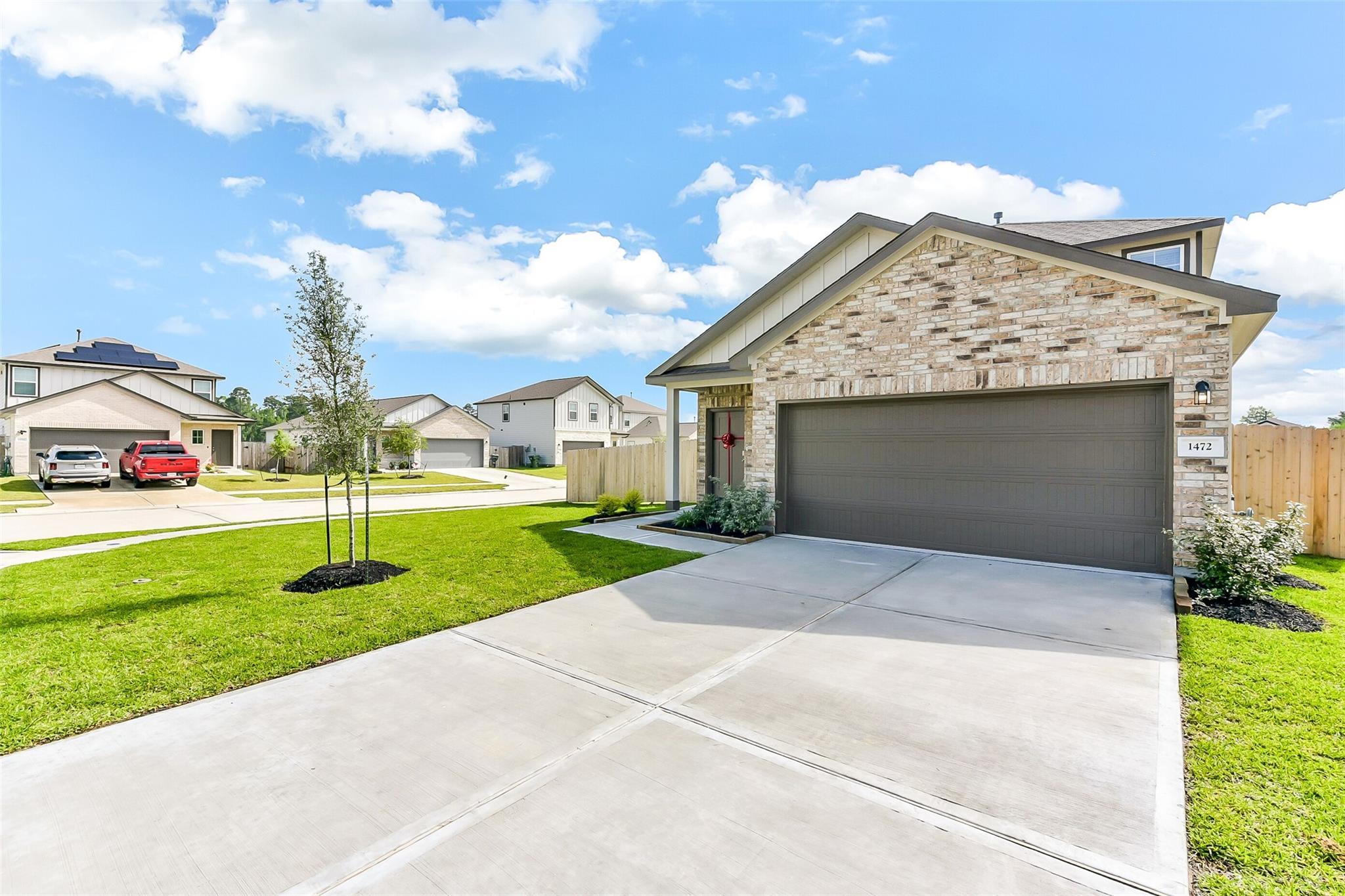 Modern two-story brick home with two-car garage, concrete driveway, and lush green lawn in The Villages at WestPointe, Dayton, Texas