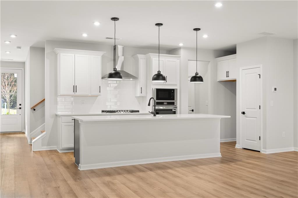 Modern white kitchen with large island, stainless steel appliances, and pendant lights in The Cary A floor plan, Winder, Georgia