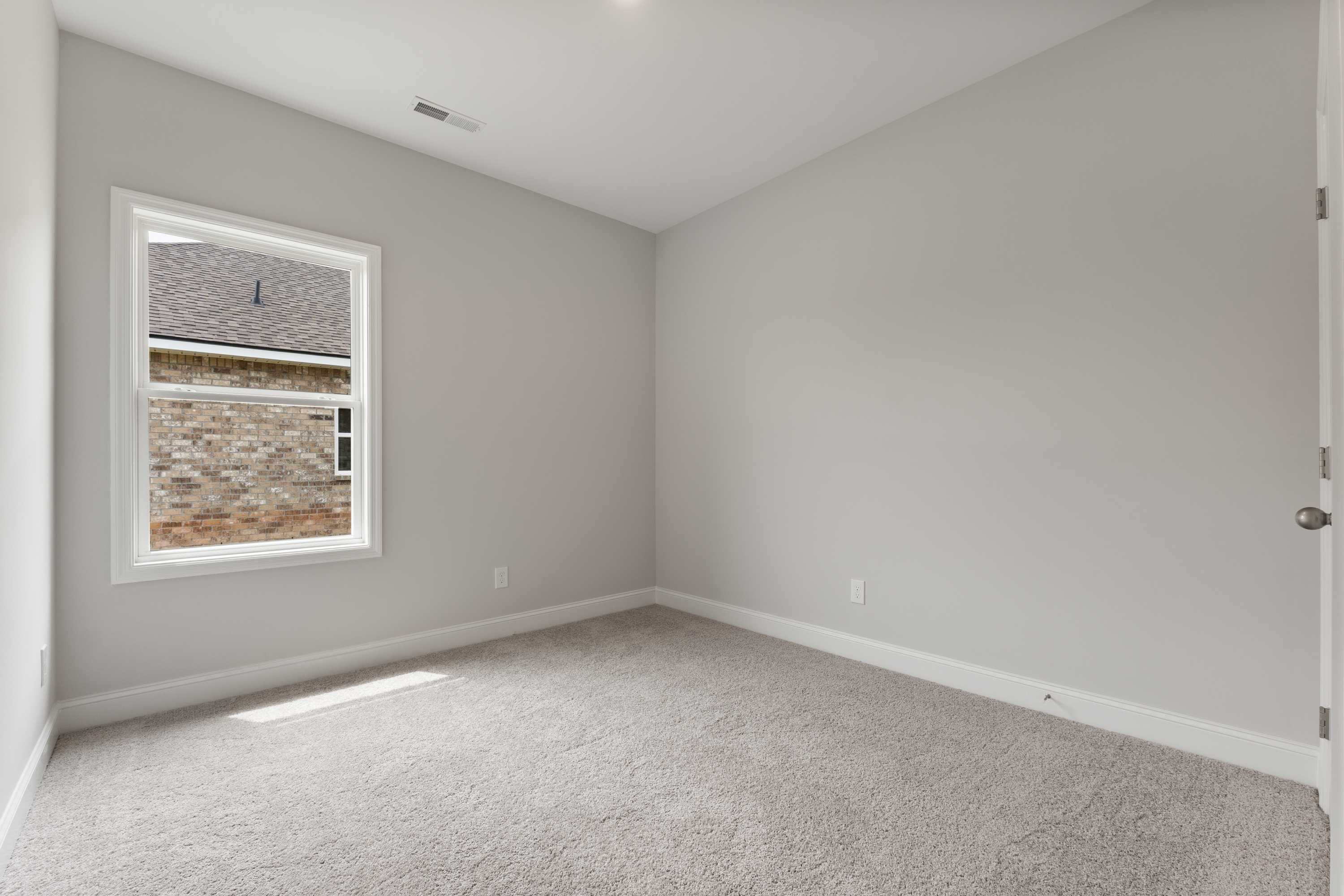 Spacious bedroom in The Butler by Davidson Homes, gray walls, carpeted floor, large window with brick exterior view