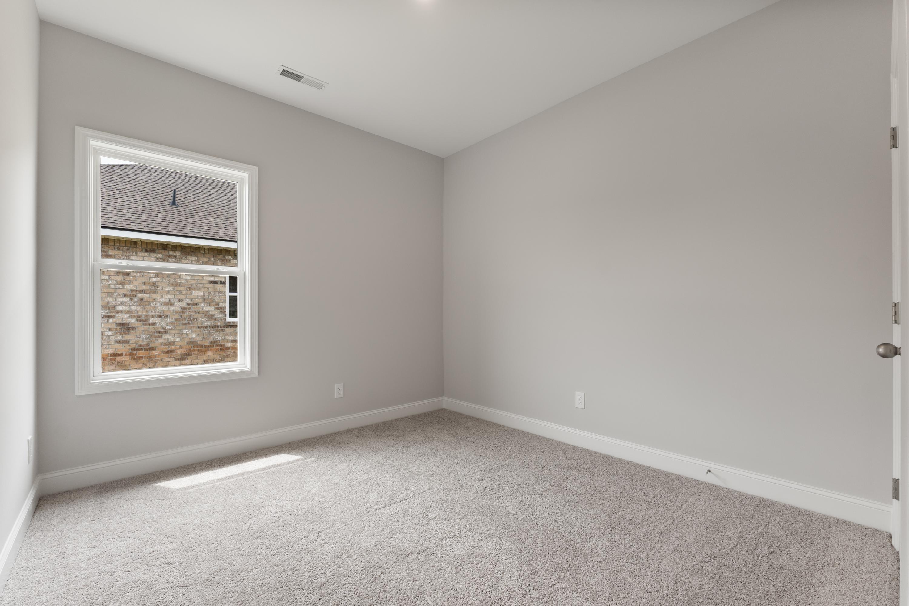 Spacious bedroom in The Butler by Davidson Homes, gray walls, carpeted floor, large window with brick exterior view