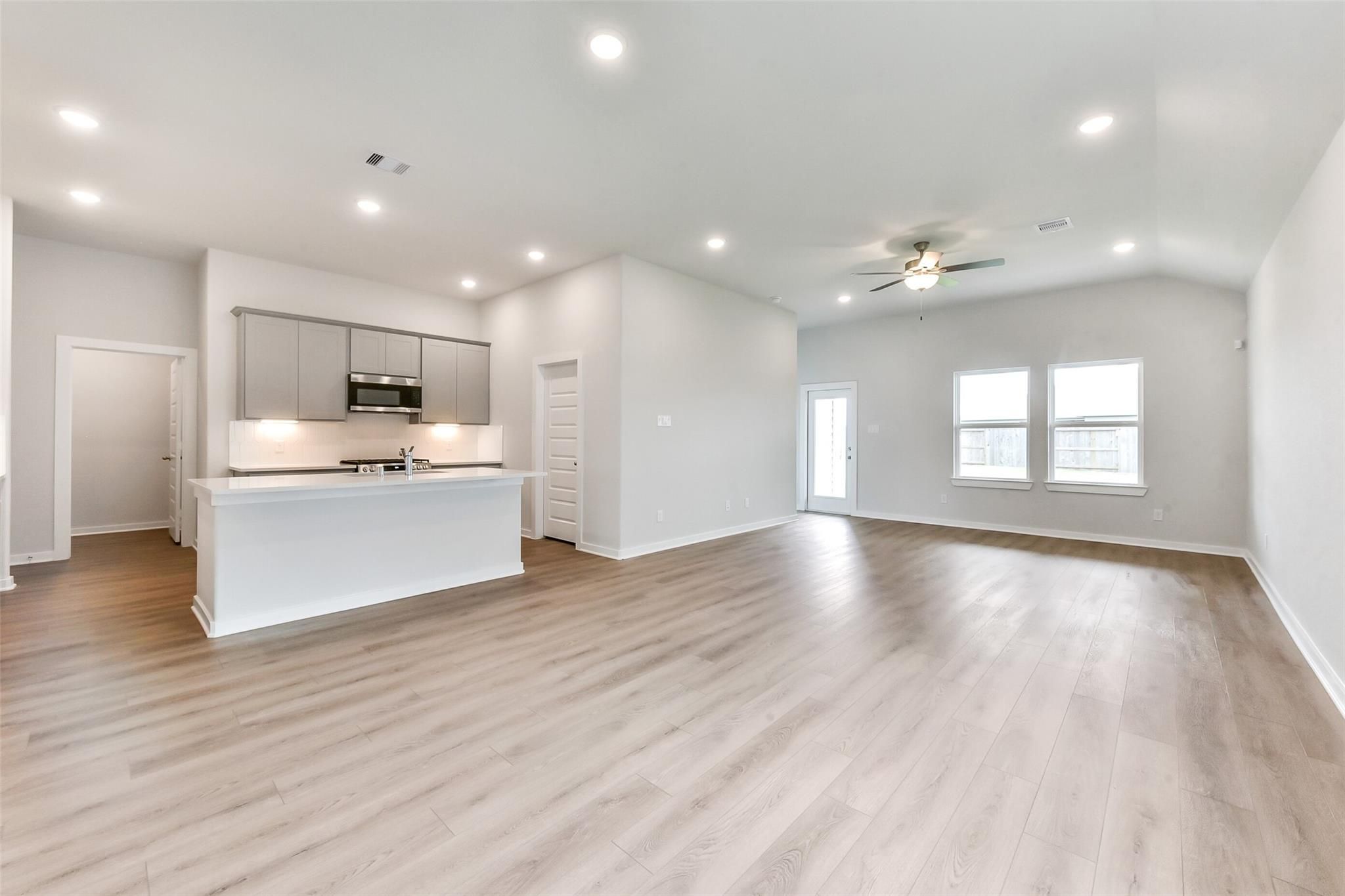 Open-concept kitchen-living area with white island, stainless appliances, ceiling fan in Davidson Homes The Laguna C, Rosharon, Texas