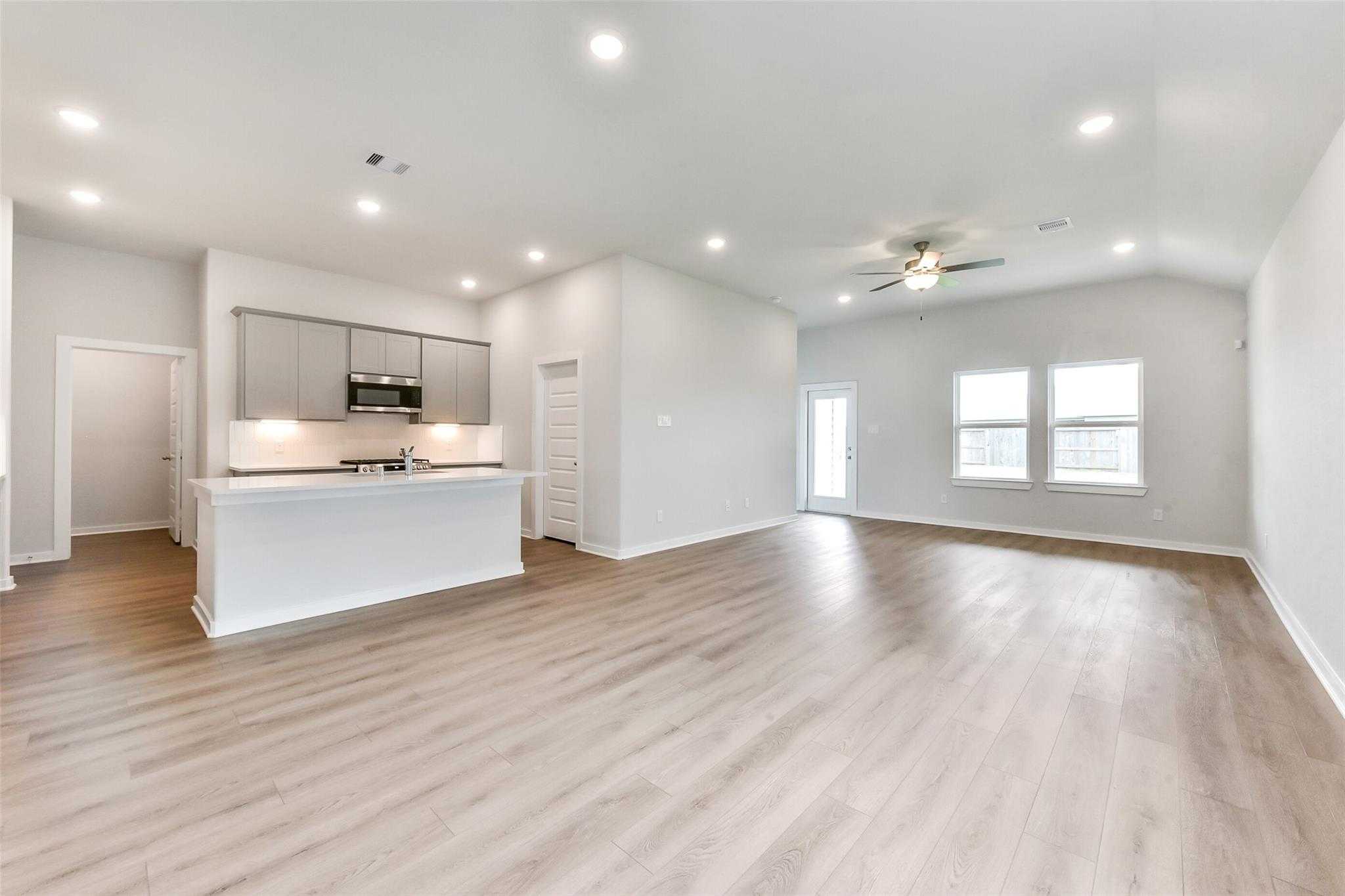 Open-concept kitchen-living area with white island, stainless appliances, ceiling fan in Davidson Homes The Laguna C, Rosharon, Texas
