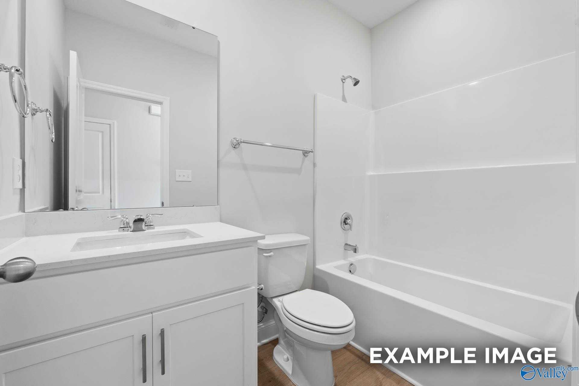 Modern white bathroom with glass shower, soaking tub, single vanity sink, toilet, and mirror in Davidson Homes The Butler, Huntsville AL