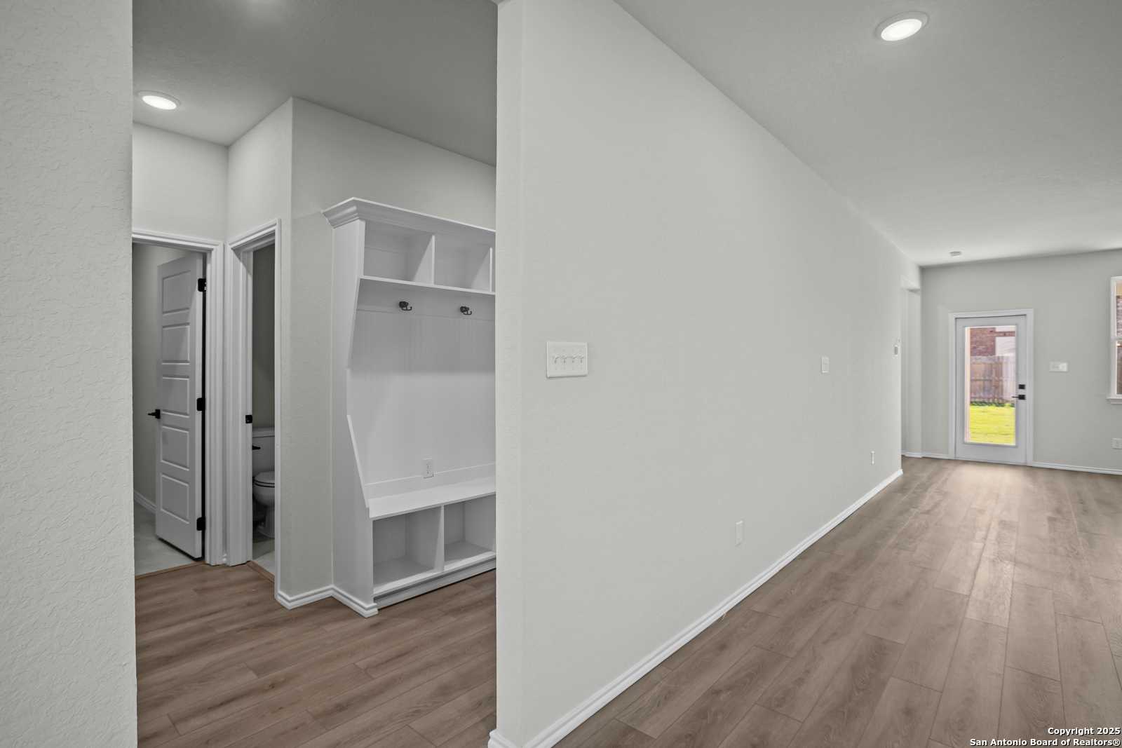 Bright mudroom with white built-in cabinetry, bench seating, and glass door to lush backyard in Davidson Homes The Douglas B, Converse, Texas