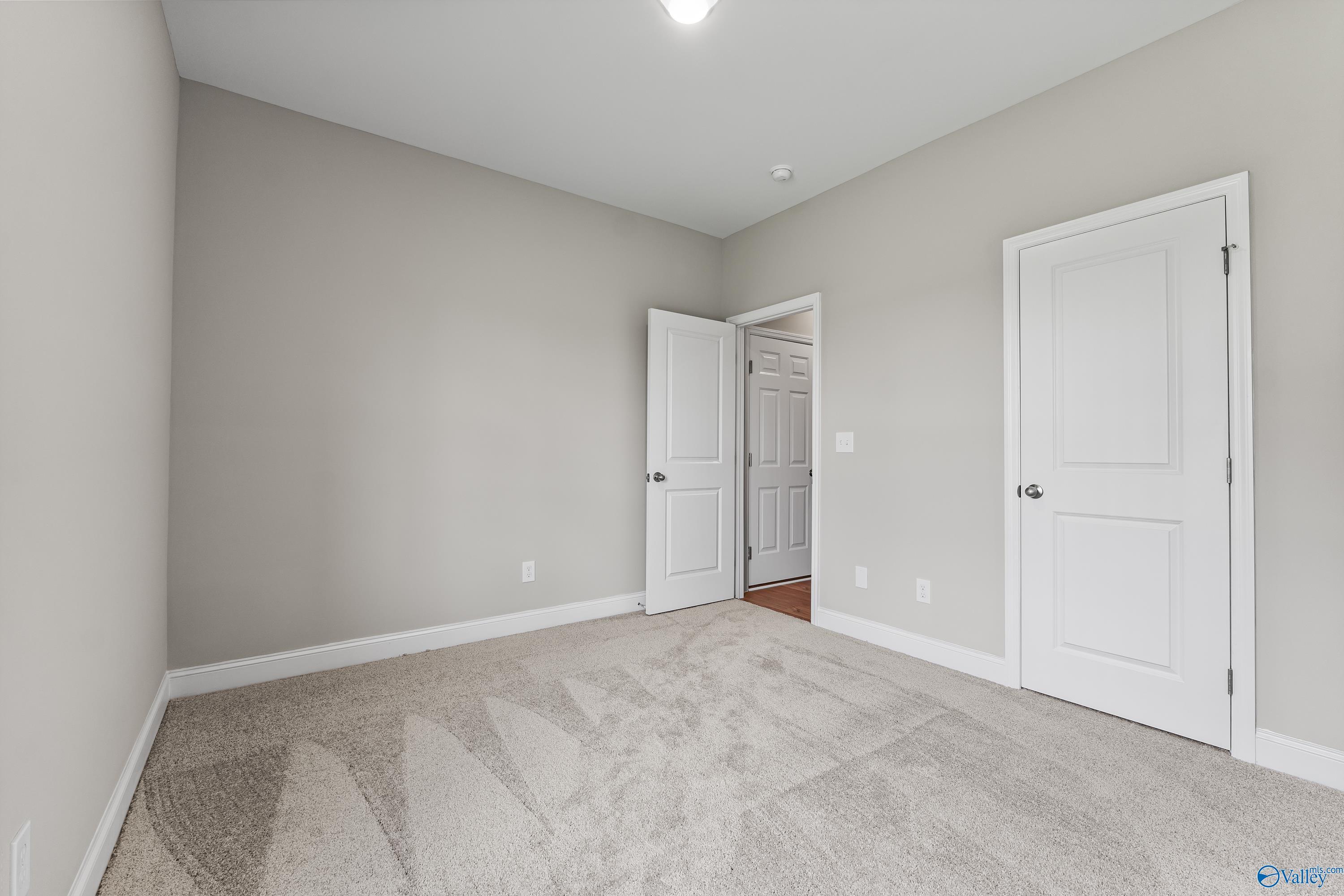 Spacious empty bedroom with light gray walls, white doors, and carpet flooring in Davidson Homes The Daphne C, Harvest, Alabama
