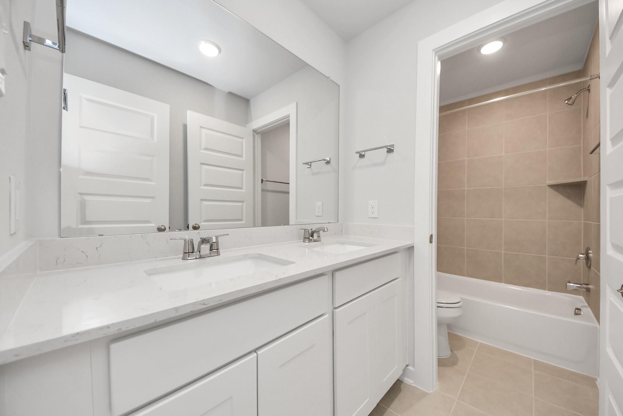 Modern bathroom with double vanity, quartz countertops, and tiled tub shower in The Blanco E floor plan, Dayton, Texas.