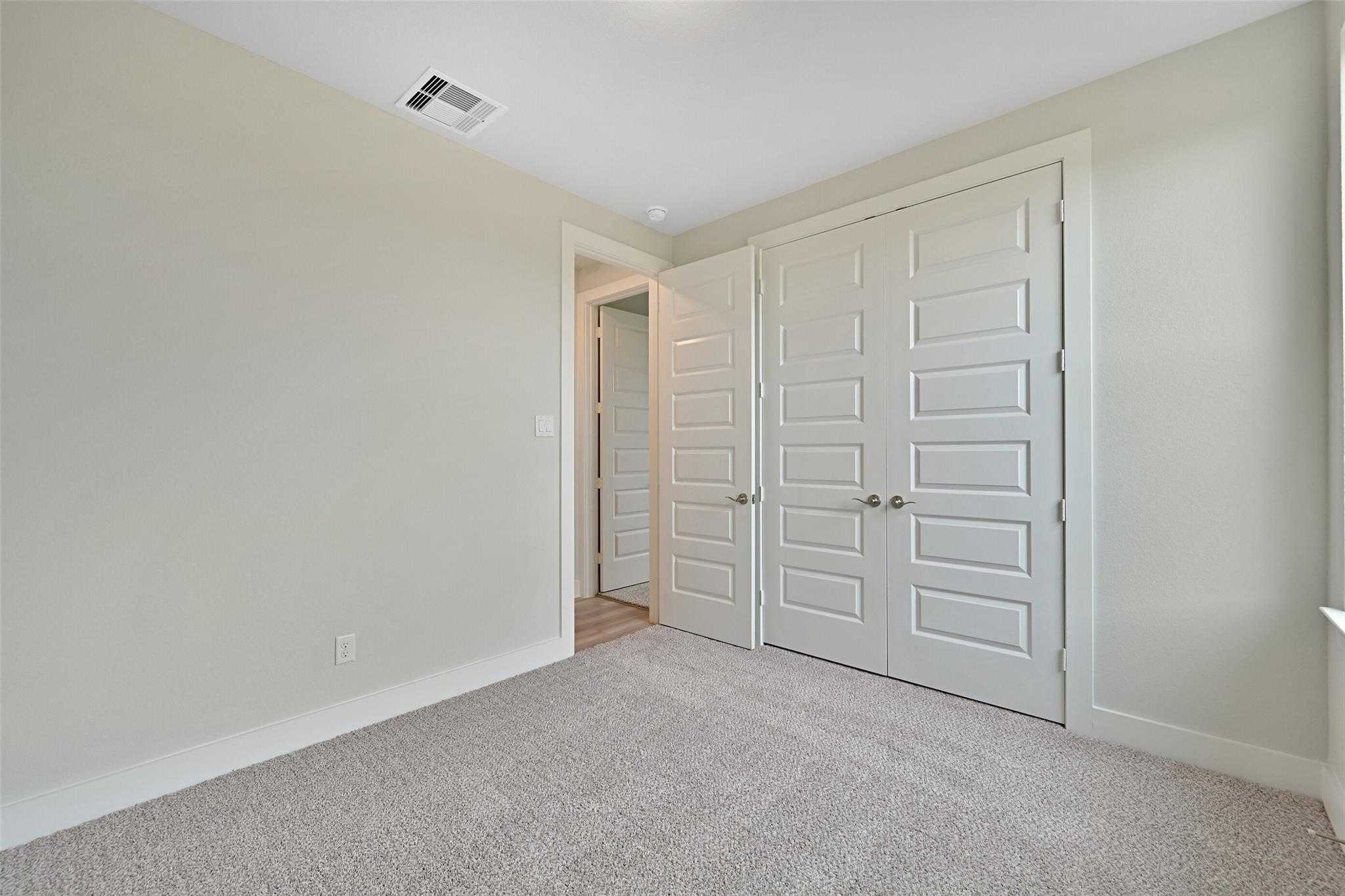 Spacious secondary bedroom with beige walls, carpet flooring, and white double-door closet in Davidson Homes The Edward A, Lago Mar, Texas City