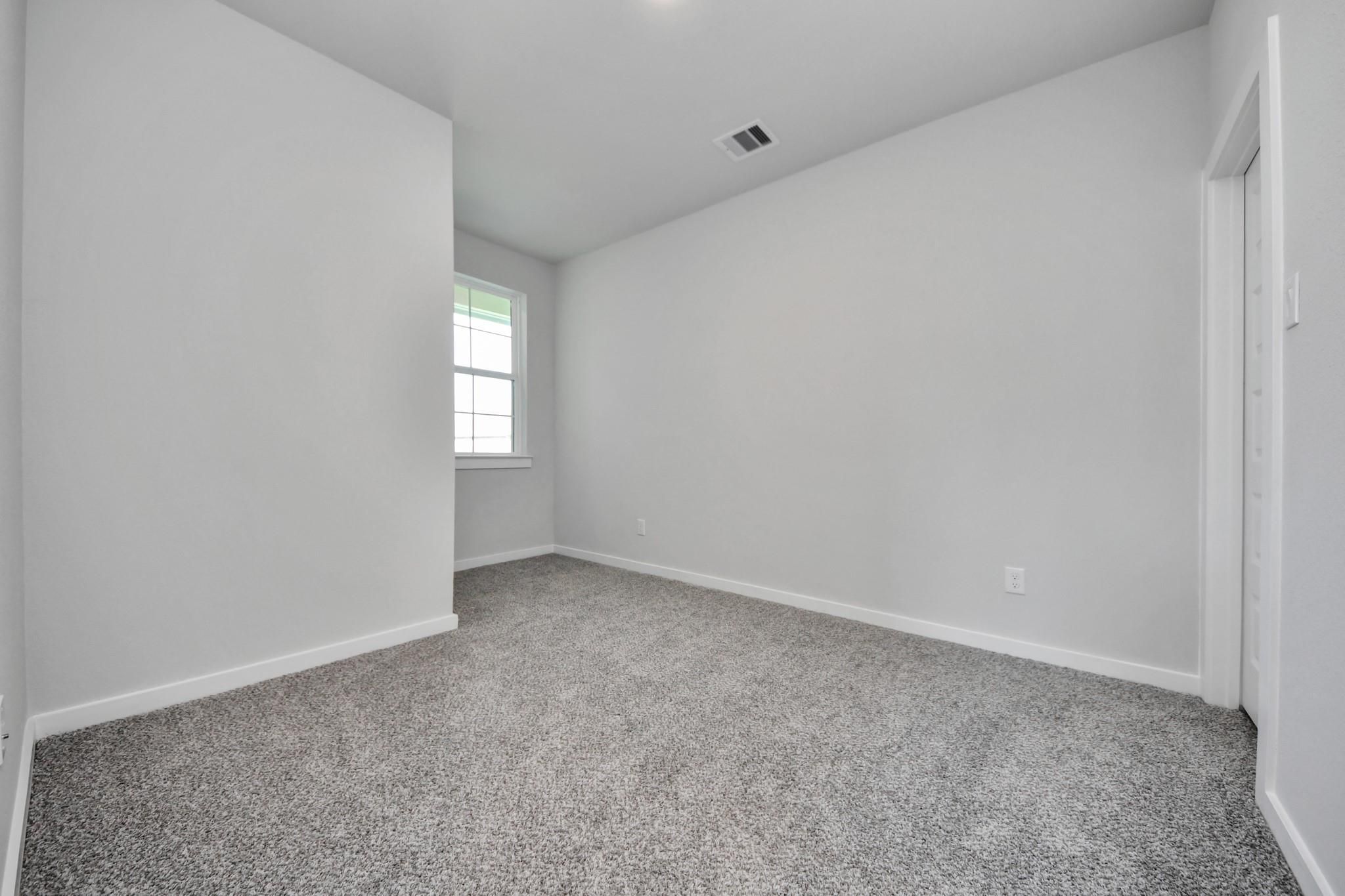 Bright, carpeted bedroom with neutral walls in The Colorado G floor plan by Davidson Homes in Emberly, Beasley, Texas.