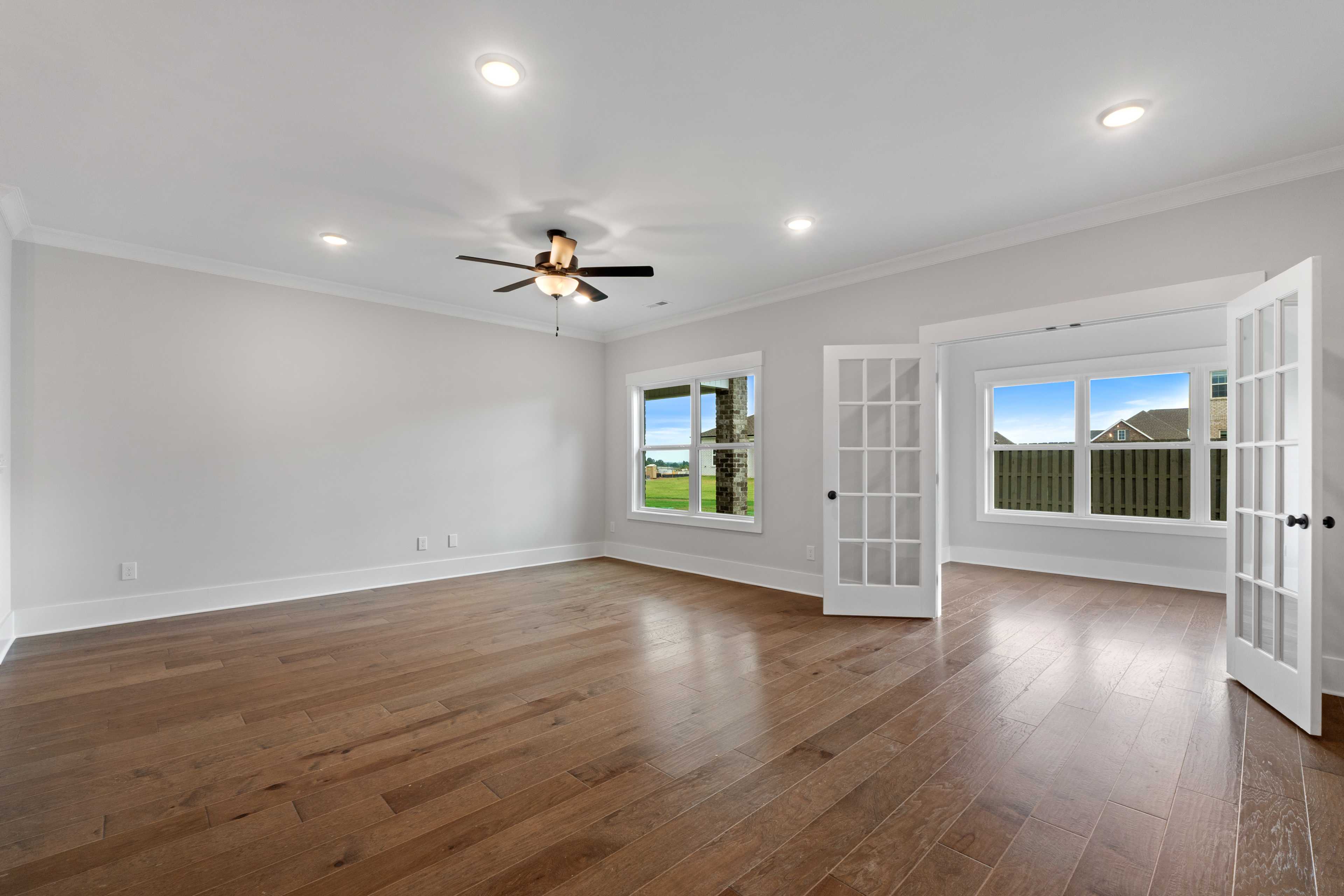 Spacious living area with hardwood floors, ceiling fan, and open French doors to green field view at The Villas at Barnett's Crossing in Madison, Alabama