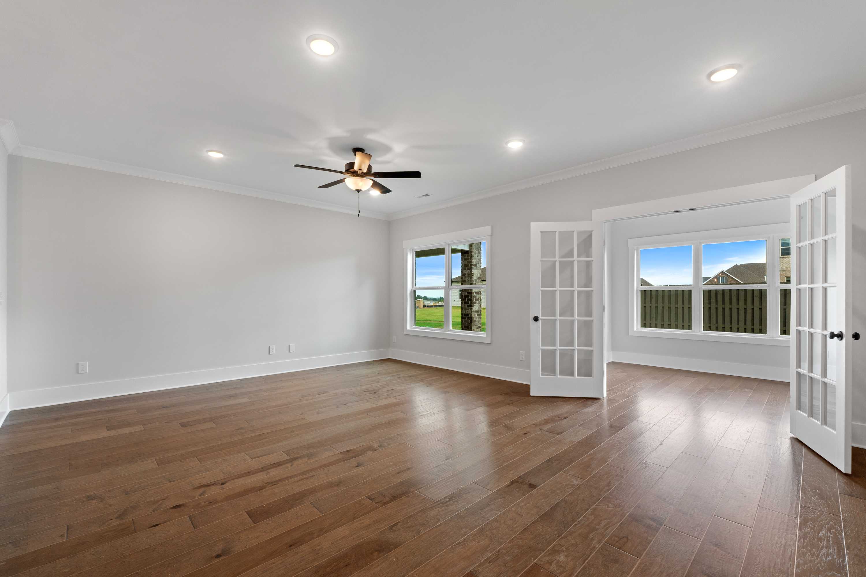 Spacious living area with hardwood floors, ceiling fan, and open French doors to green field view at The Villas at Barnett's Crossing in Madison, Alabama