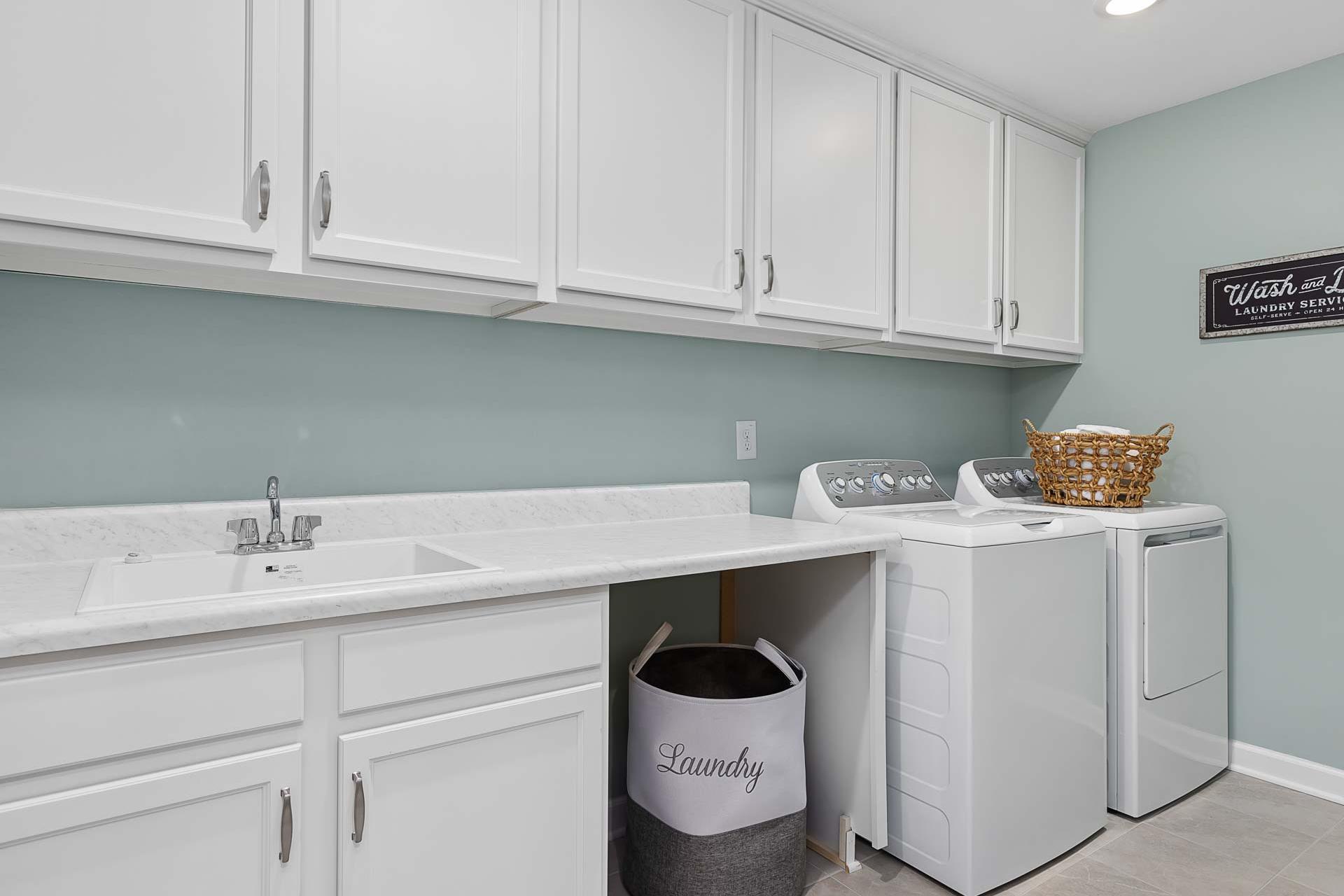 Spacious laundry room at Highland Forest in Fuquay-Varina NC with white cabinets, washer, dryer, utility sink and blue accent wall