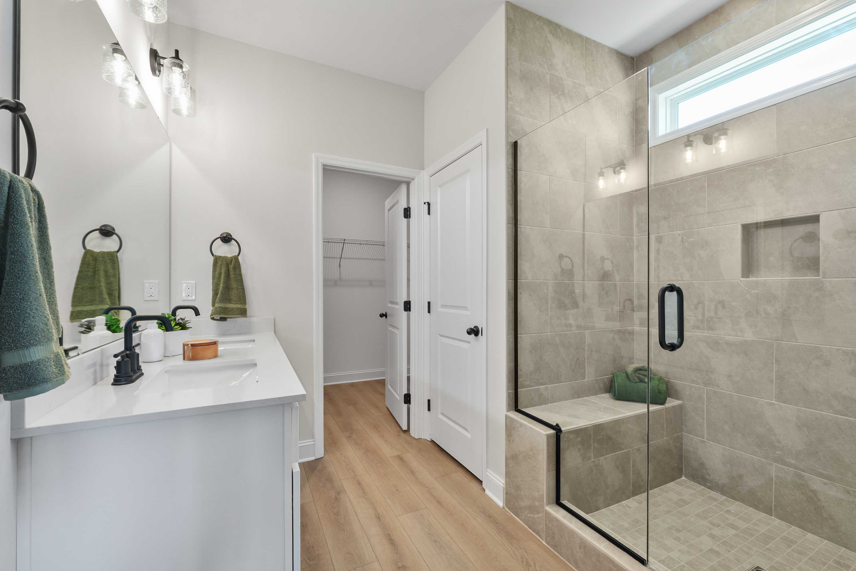 Spacious modern bathroom in Ramsay Cove, Owens Cross Roads AL with white vanity, walk-in tiled shower, green towels and hardwood floors