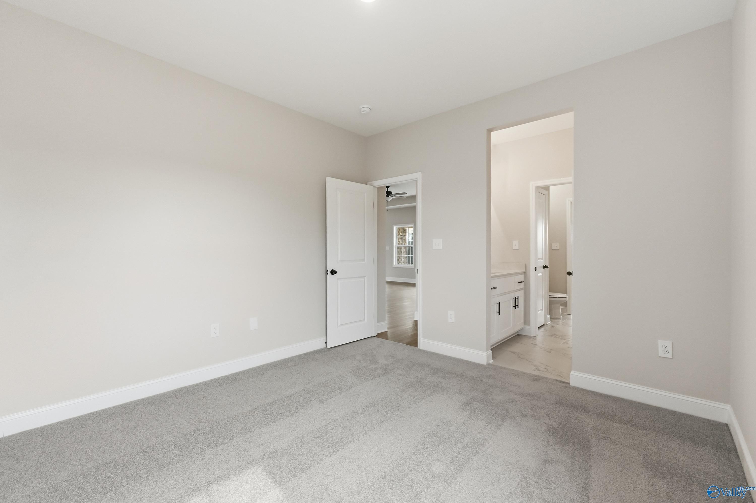 Spacious carpeted bedroom with neutral walls and attached bath featuring vanity sink in Davidson Homes The Finleigh, Meridianville AL