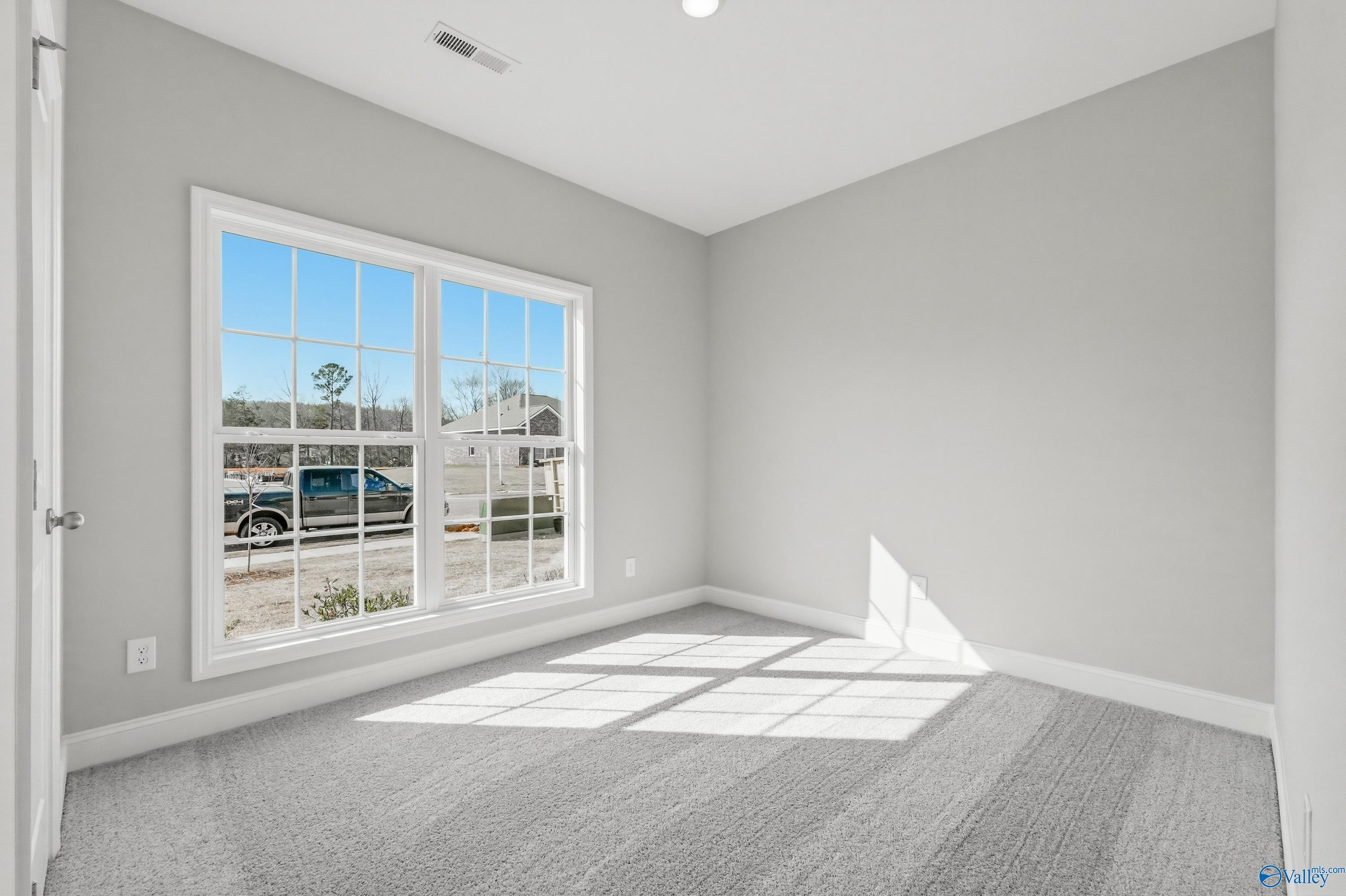Bright secondary bedroom with large window overlooking new homes, gray walls and carpet in The Asheville plan, Huntsville AL