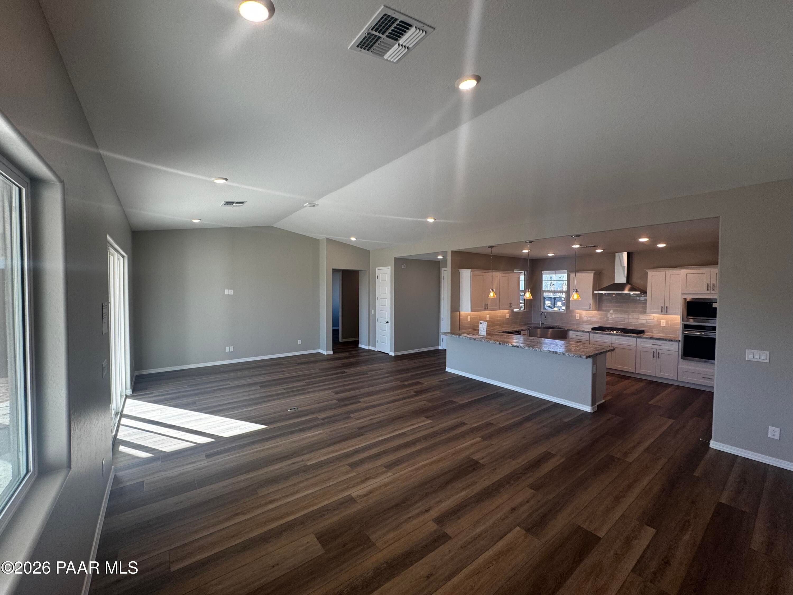 Spacious open-concept kitchen and living area with hardwood floors, white cabinets, and large windows in Davidson Homes Daybreak B, Prescott AZ