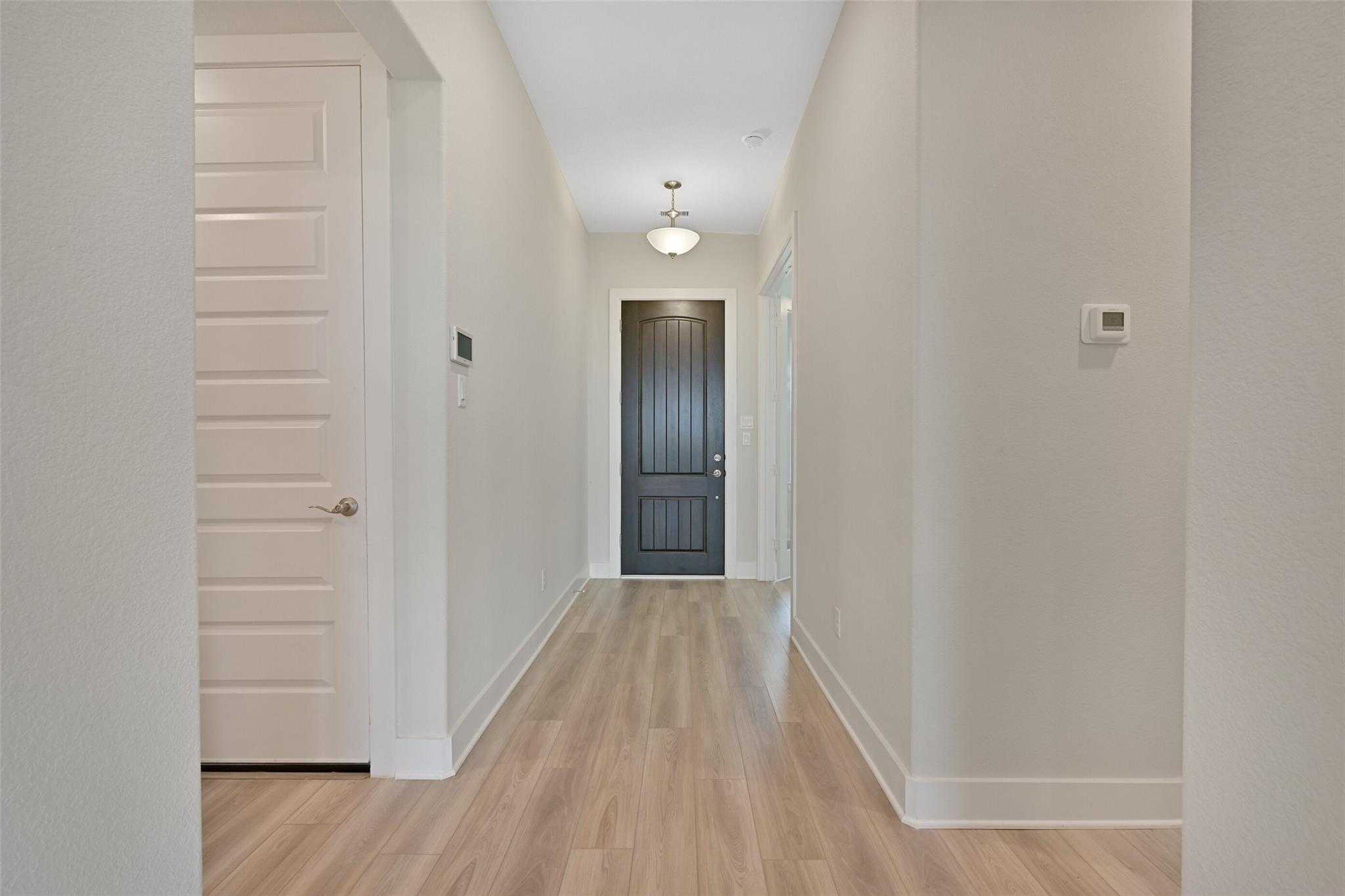 Elegant hallway with light oak floors, white walls, and dark entry door in Davidson Homes The Edward A, Lago Mar, Texas City