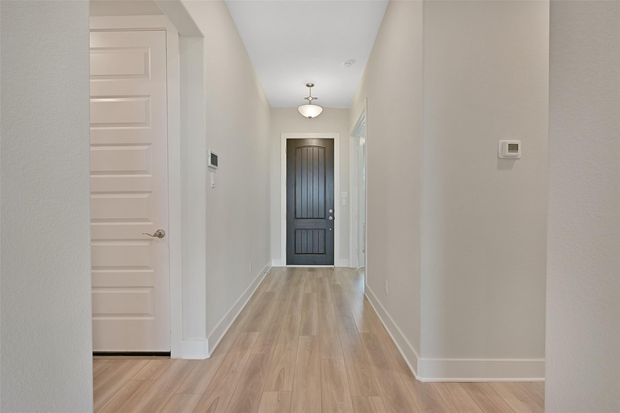 Elegant hallway with light oak floors, neutral walls, white doors, and dark entry in Davidson Homes The Edward A, Lago Mar, Texas City