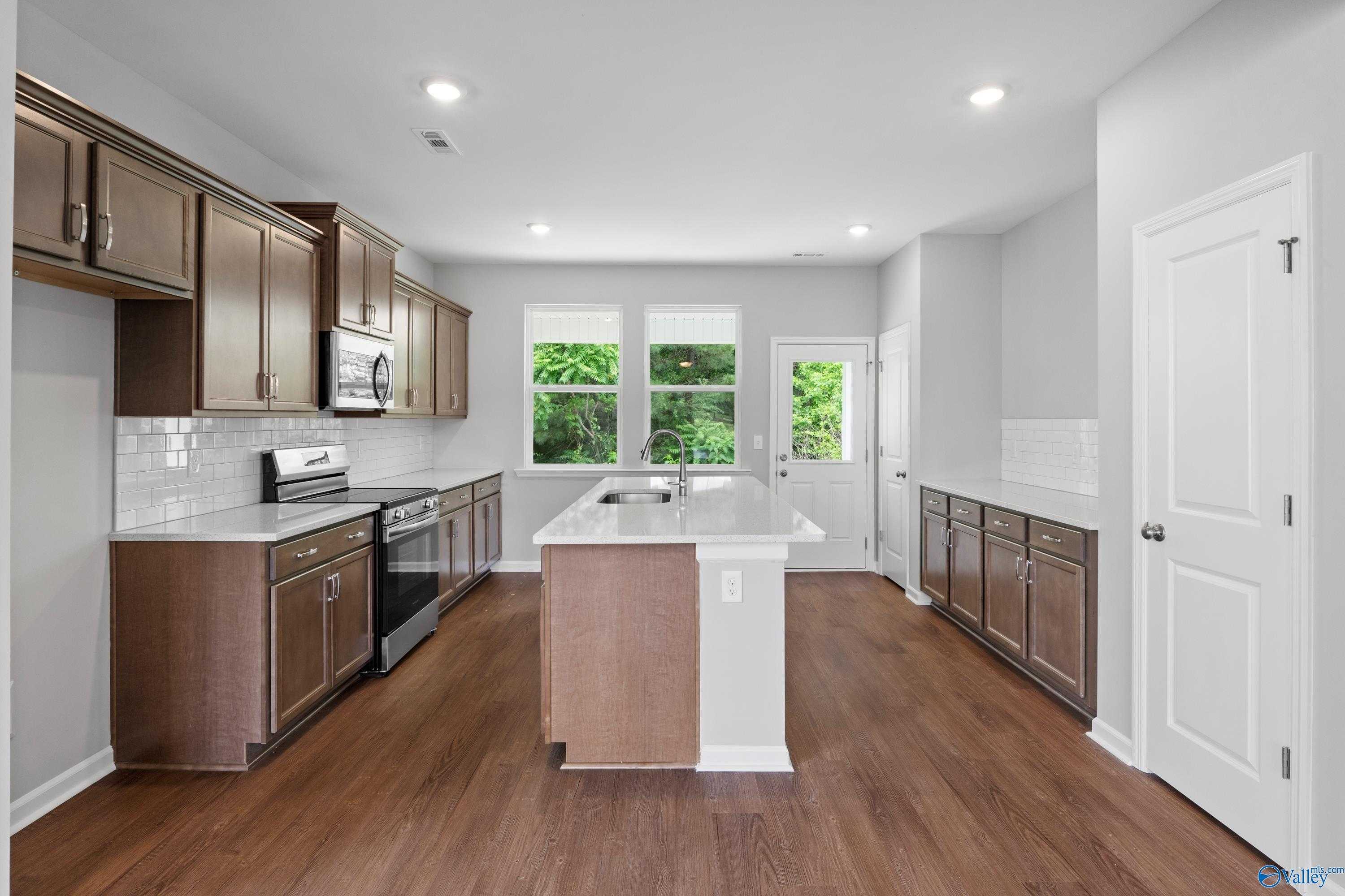 Modern kitchen featuring large center island, stainless appliances, subway tile backsplash, and hardwood floors in Davidson Homes The Stella, Hazel Green, AL