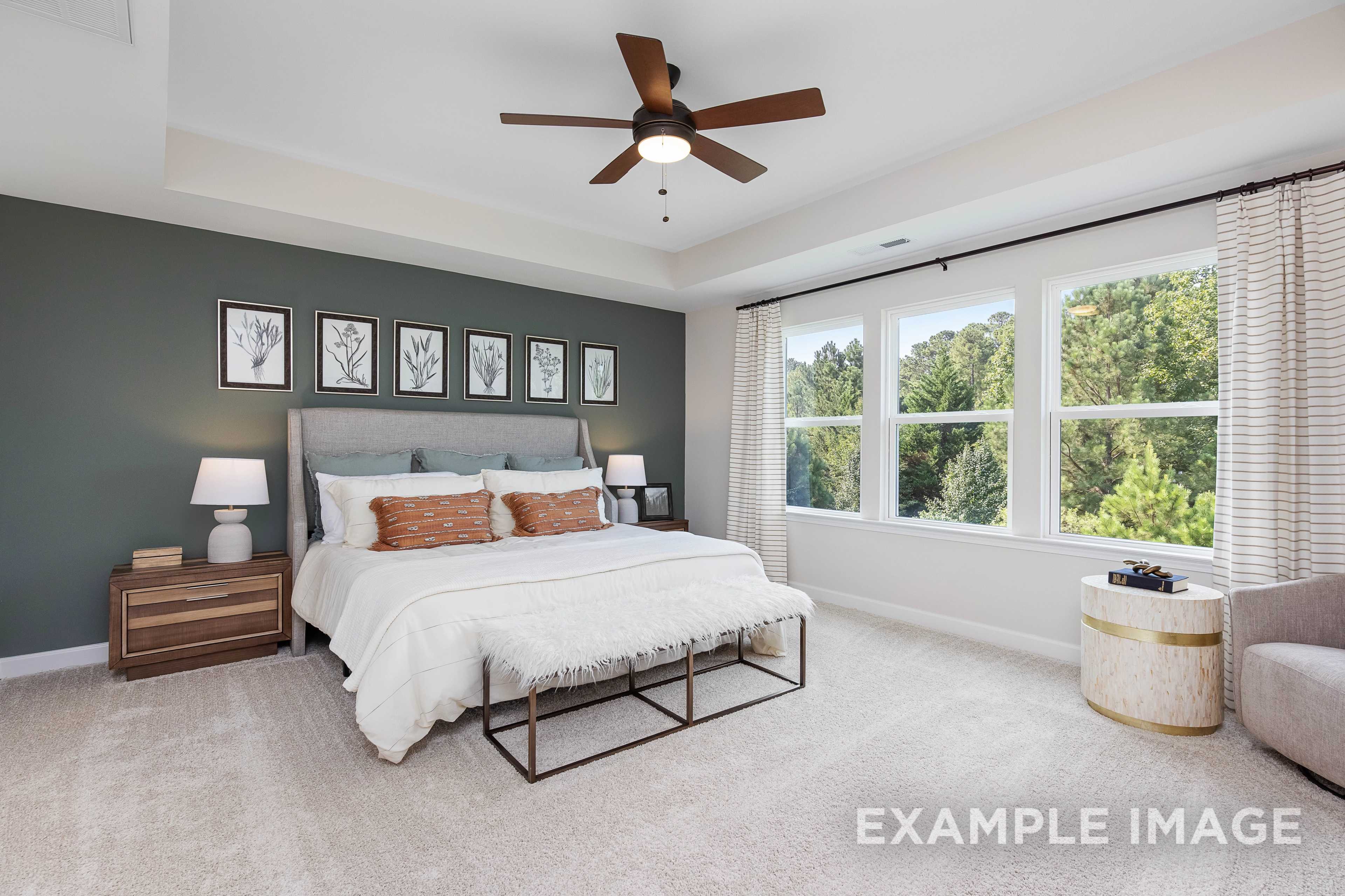 Spacious master bedroom in The Willow B with gray accent wall, king bed, large windows overlooking woods, ceiling fan