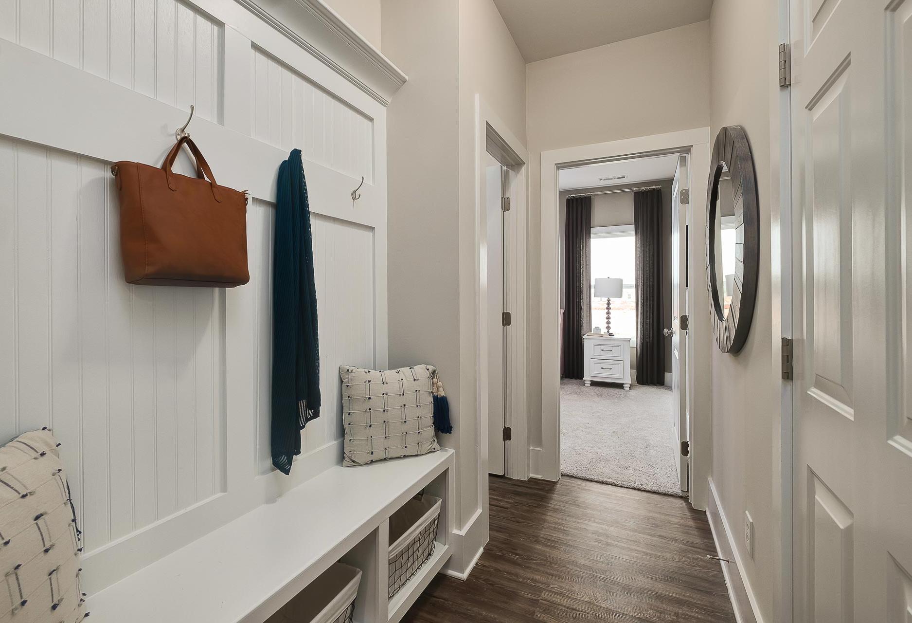 Spacious mudroom in The Everett home design with white shiplap walls, built-in bench, leather handbag on hooks, and hallway to bedroom