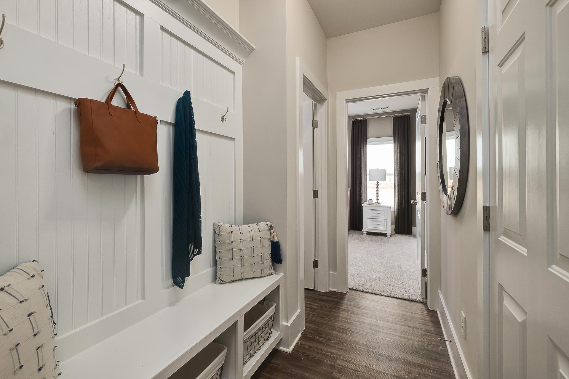 Spacious mudroom in The Everett home design with white shiplap walls, built-in bench, leather handbag on hooks, and hallway to bedroom