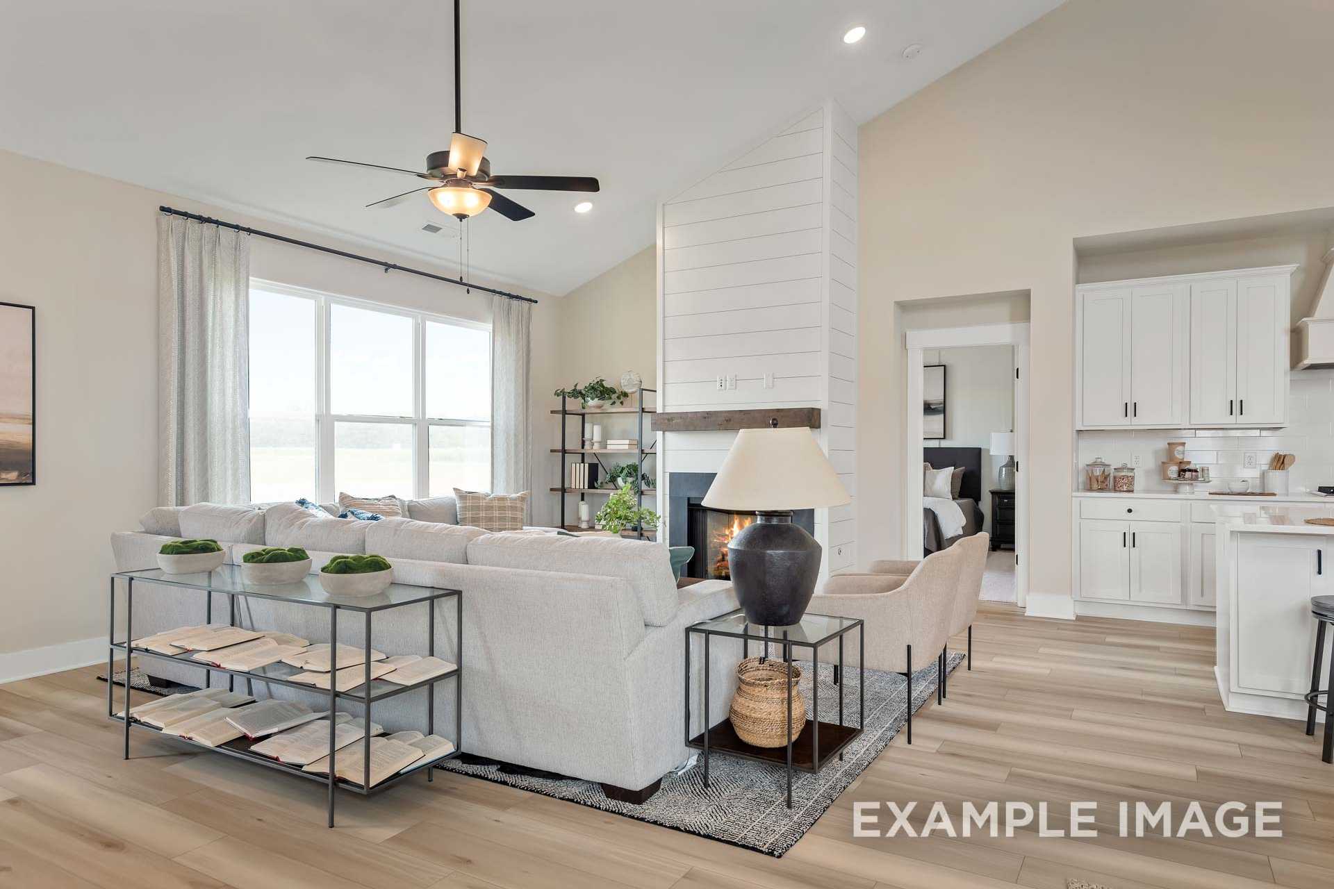 Spacious Ridgeport B living room with vaulted ceiling, shiplap fireplace, gray sectional sofa, plants, and open white kitchen