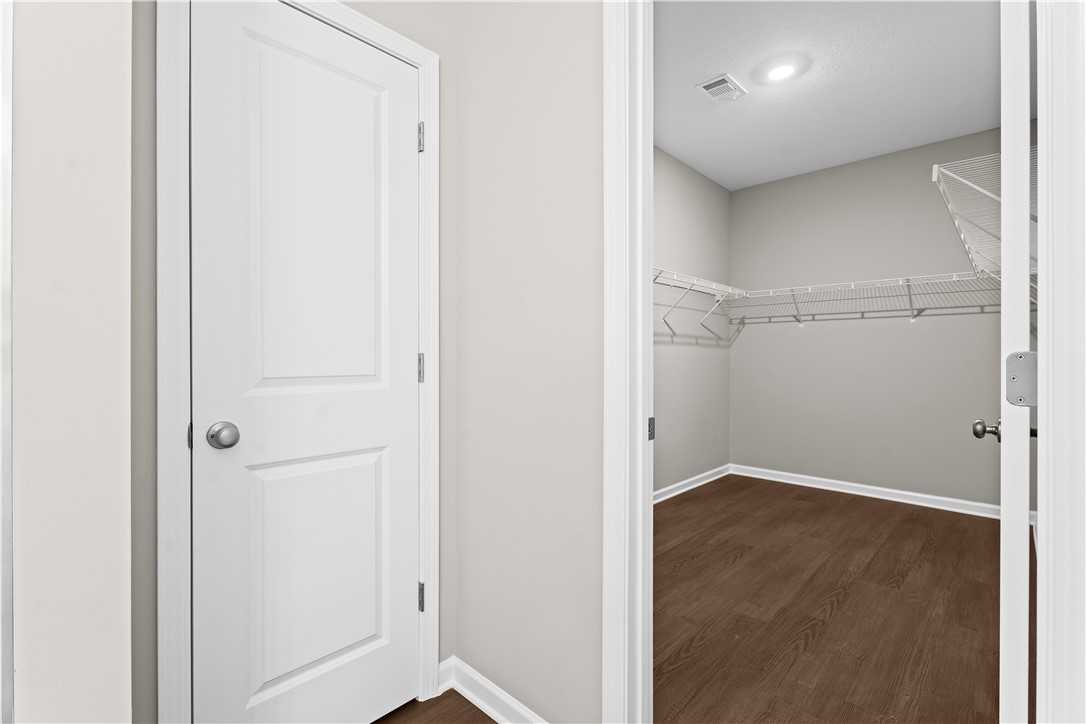 Spacious walk-in closet with beige walls, wooden floors, and built-in shelving in Evermore Homes The Orion, Cusseta, Alabama