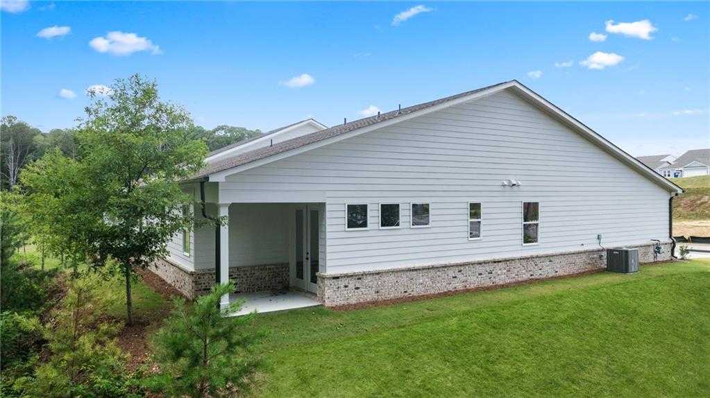 Side view of The Daphne B single-story home by Davidson Homes, white siding, brick accents, covered porch, lush lawn in Kelly Preserve, Loganville, GA