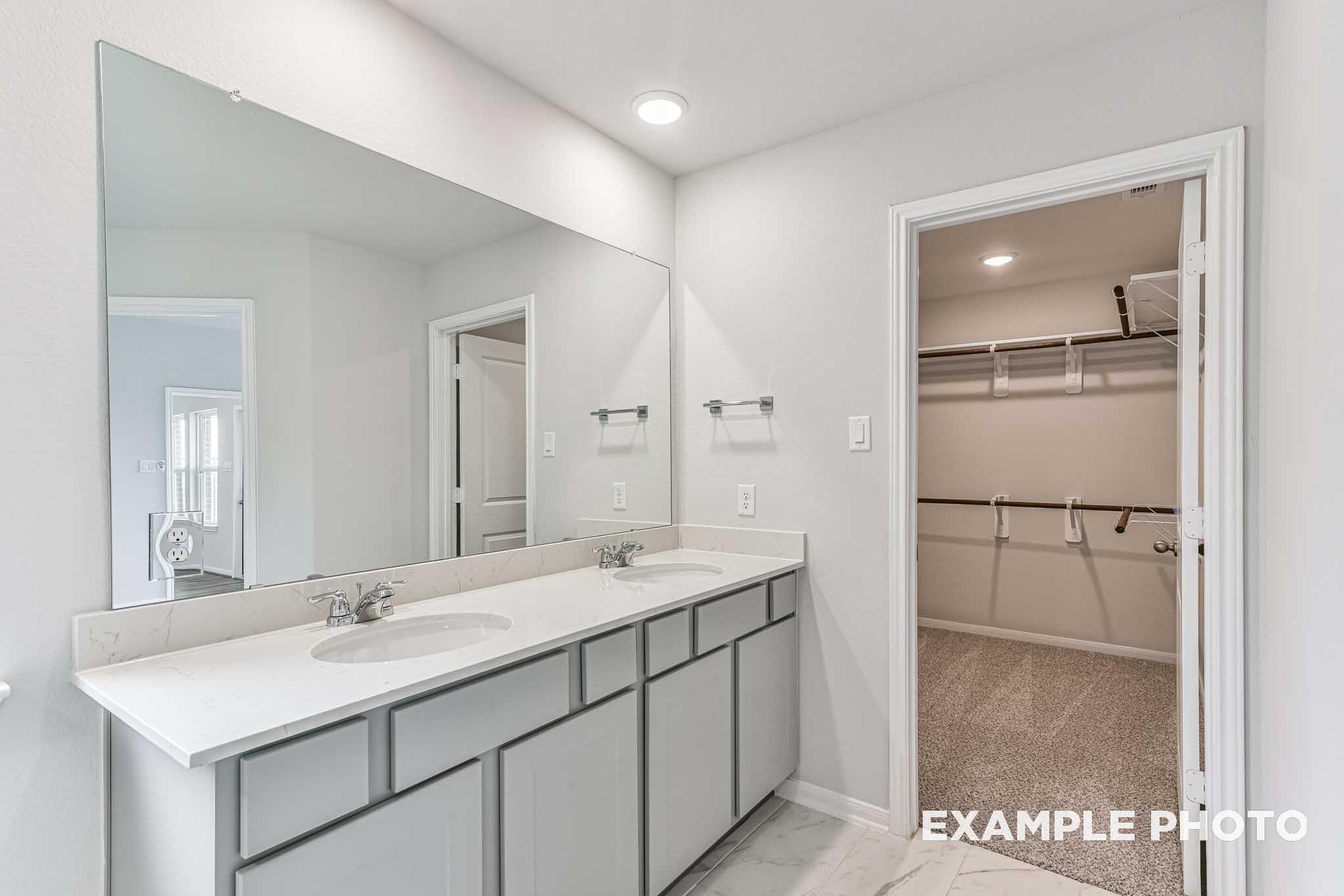 Master bathroom in The Costa A featuring double vanity with gray cabinets, large mirrors, and adjacent walk-in closet