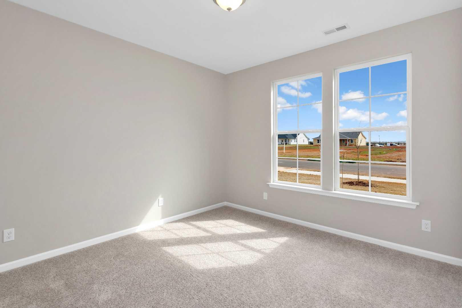 Bright secondary bedroom in The Orion by Evermore Homes with gray walls, carpet floor, and large windows overlooking Cusseta neighborhood