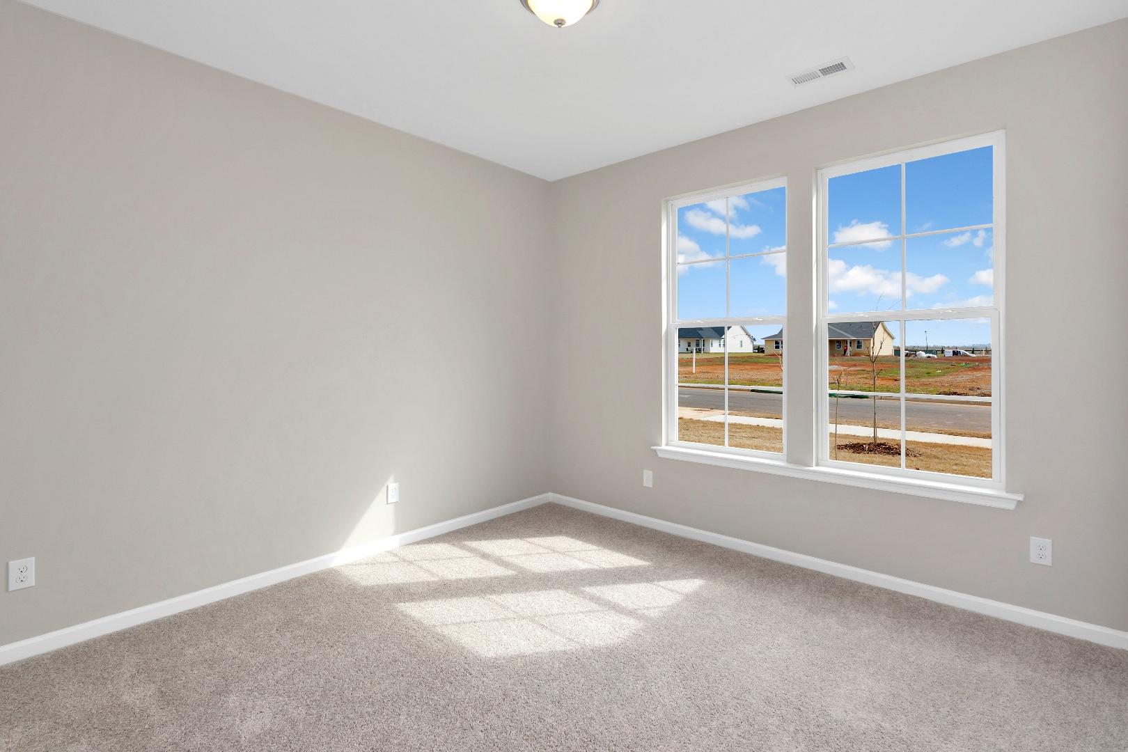 Bright secondary bedroom in The Orion by Evermore Homes with gray walls, carpet floor, and large windows overlooking Cusseta neighborhood
