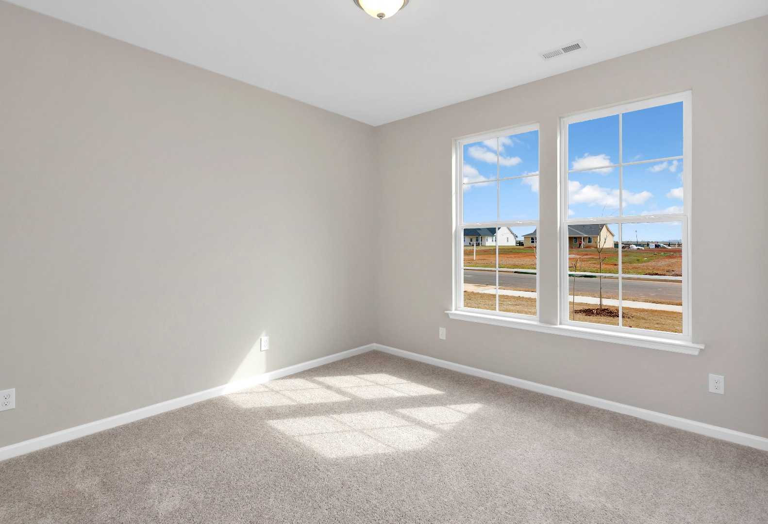 Bright secondary bedroom in The Orion by Evermore Homes with gray walls, carpet floor, and large windows overlooking Cusseta neighborhood