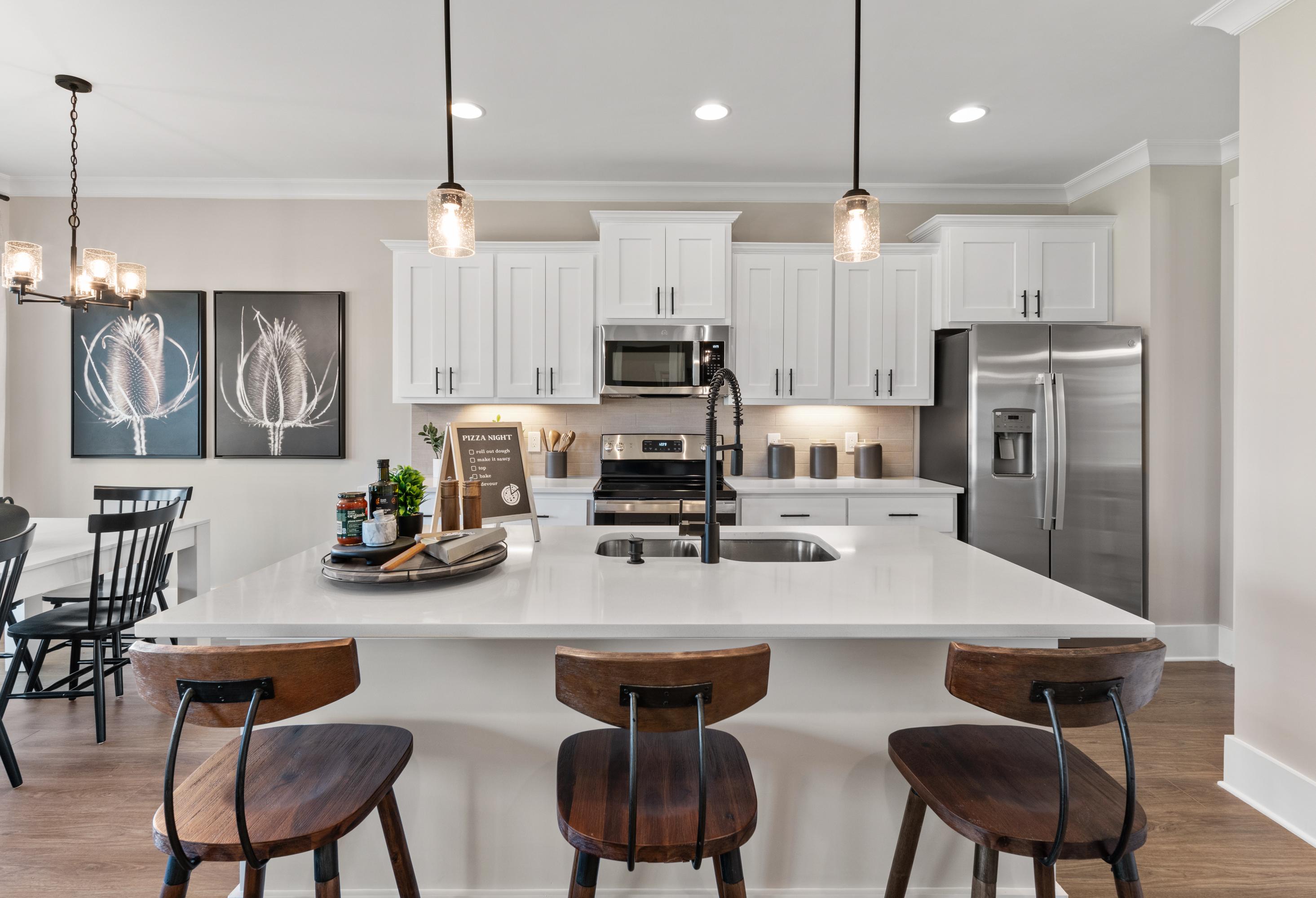 Modern kitchen in The Shelby A by Davidson Homes featuring white cabinets, large island with bar stools, stainless steel appliances, and pendant lights