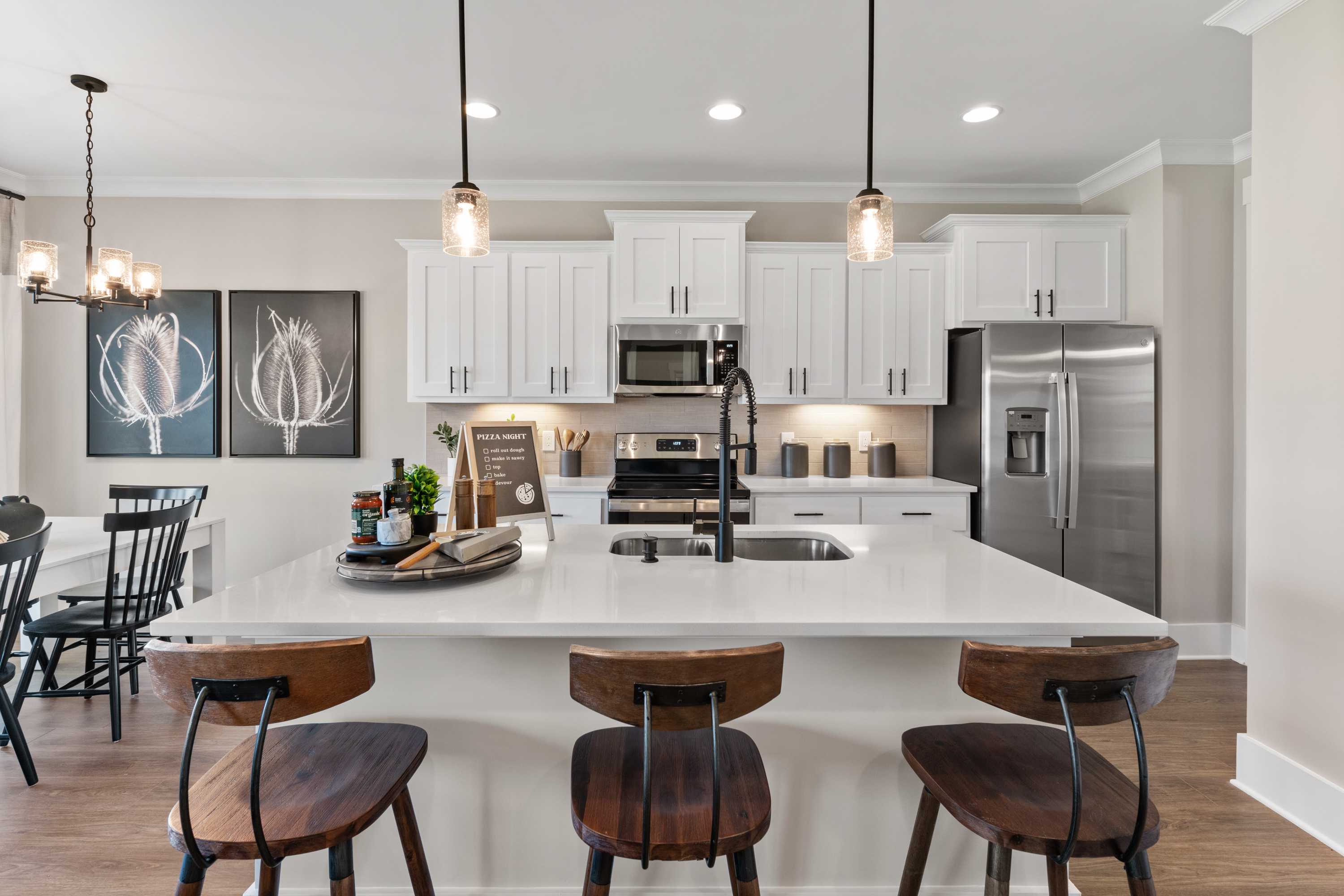 Modern kitchen in The Shelby A by Davidson Homes featuring white cabinets, large island with bar stools, stainless steel appliances, and pendant lights