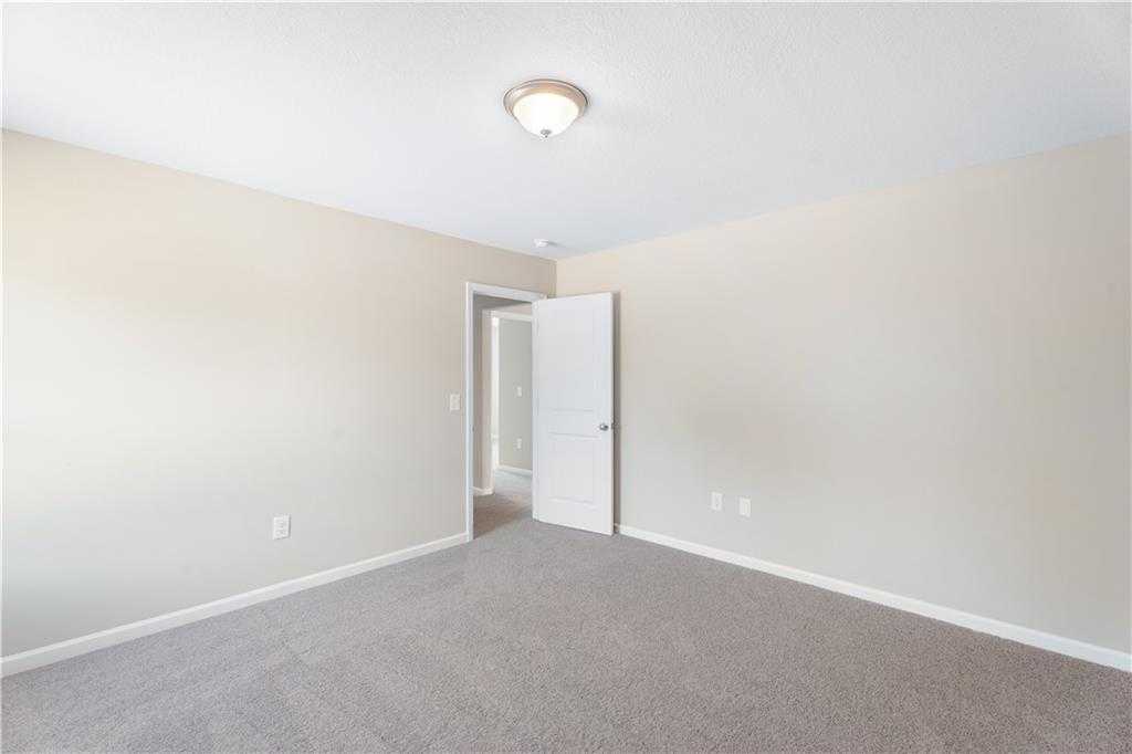 Empty bedroom with beige walls, gray carpet flooring, and open doorway in Evermore Homes The Washington, Phenix City, Alabama
