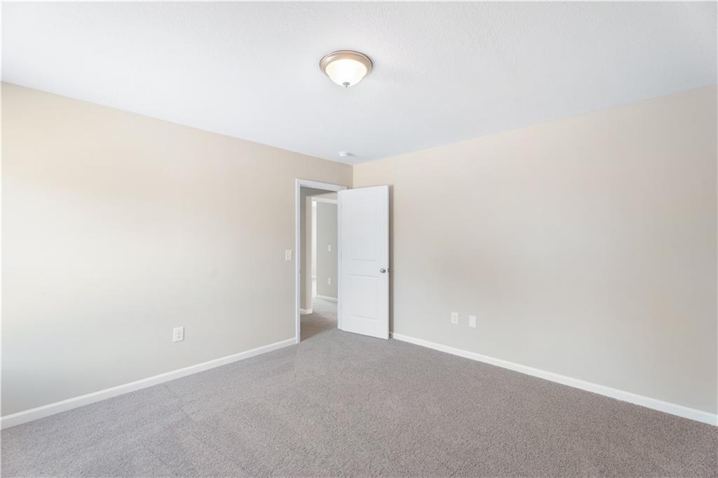 Empty bedroom with beige walls, gray carpet flooring, and open doorway in Evermore Homes The Washington, Phenix City, Alabama