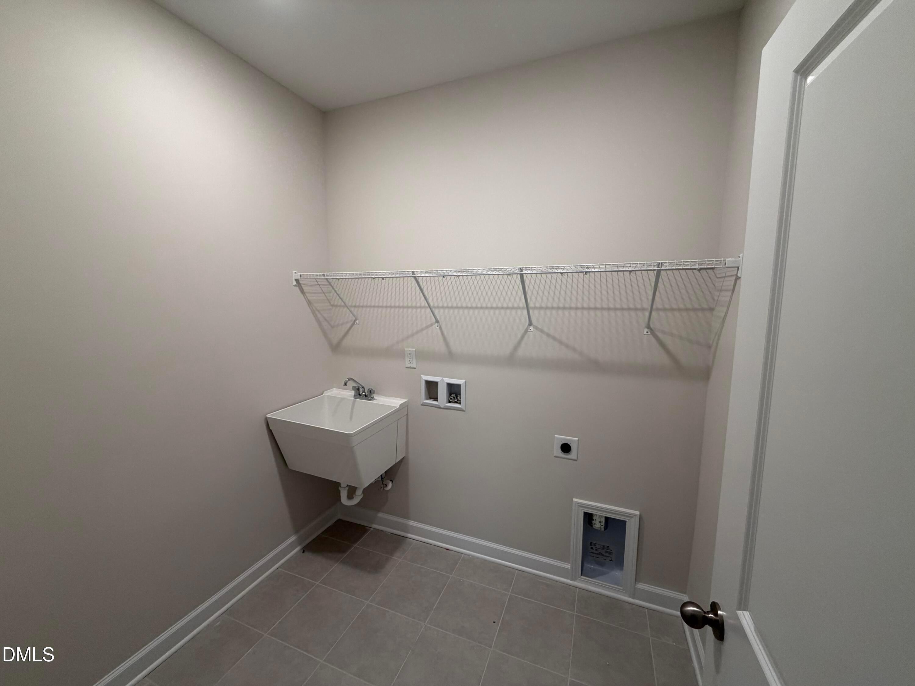 Functional laundry room with utility sink, wire shelving, and beige walls in Davidson Homes The Ash B, Wellers Knoll, Lillington, NC