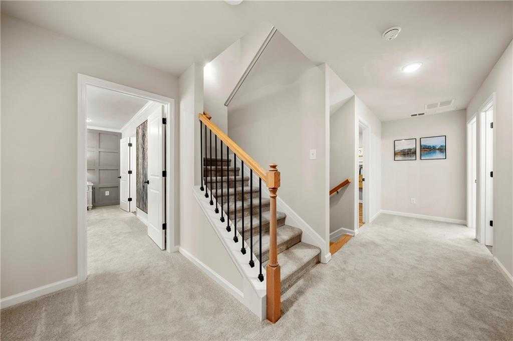 Elegant upstairs hallway featuring wooden staircase with black balusters and bedroom doors in Davidson Homes The Hickory B, Riverwood, Dallas, GA