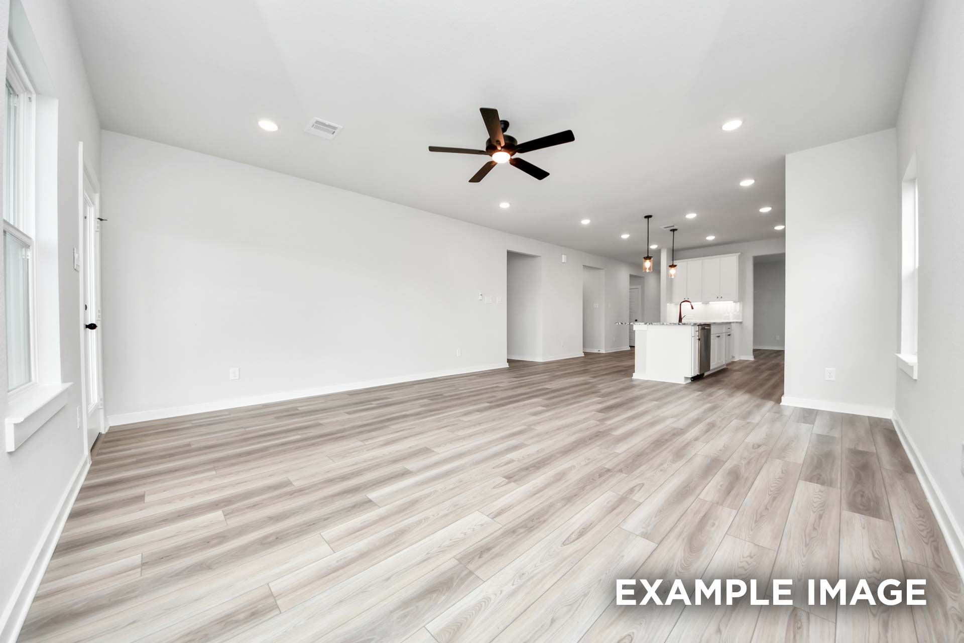 Open-concept living area in The Sorrento with wood-look flooring, ceiling fan, and views of the modern kitchen.