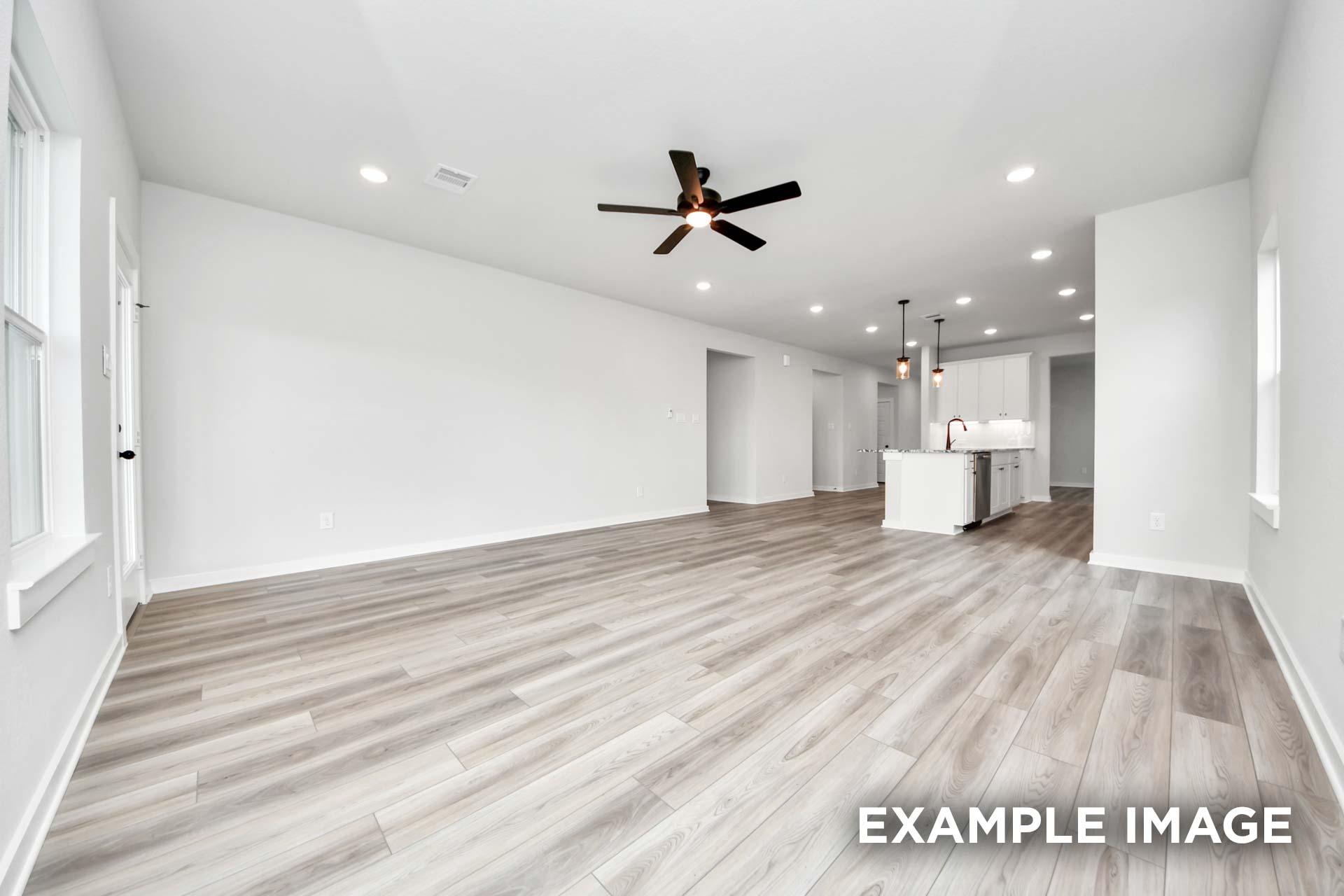 Open-concept living area in The Sorrento with wood-look flooring, ceiling fan, and views of the modern kitchen.